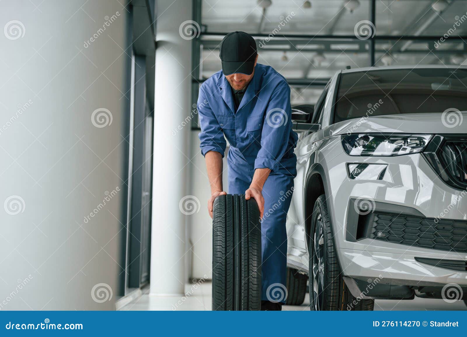 Front View, Moving the Tire. Man in Blue Uniform is Working in the Car