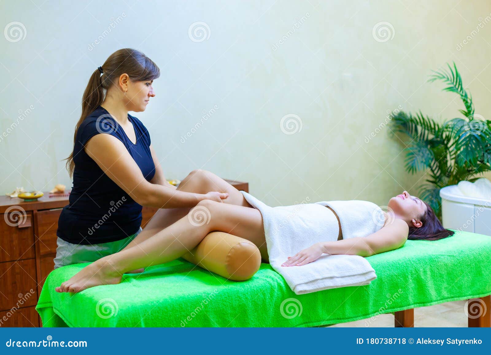 Front View Of Professional Massage Therapist Giving Massage On Woman Legs In The Spa Salon Stock