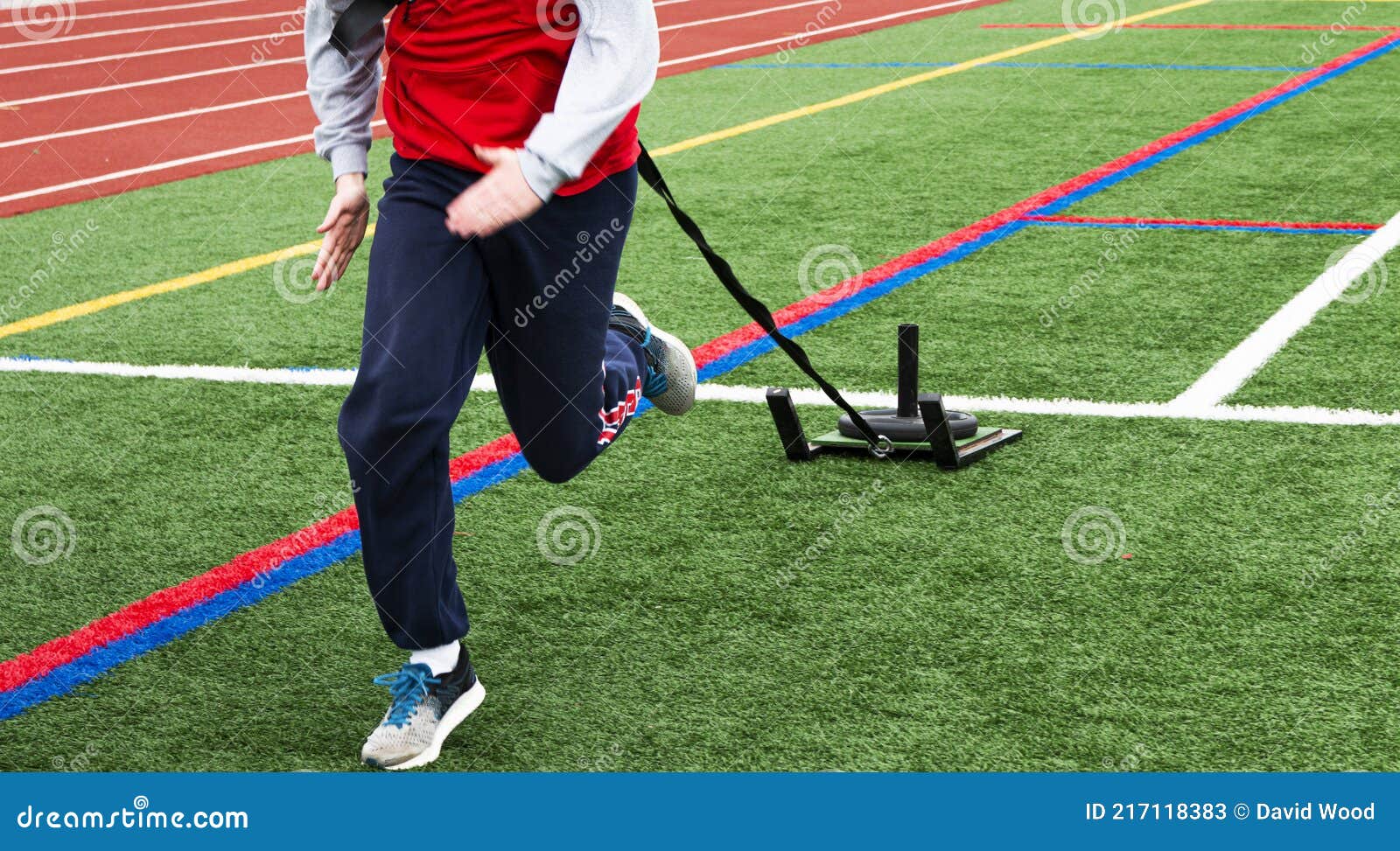 Front View of Runner Pulling a Weighted Sled on a Field Next To a Track