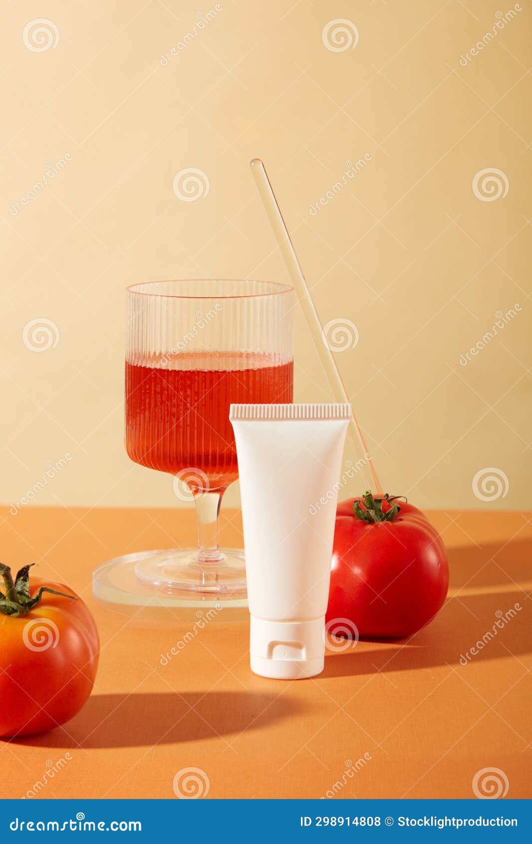 front view of an unlabeled cosmetic tube and a glass of tomato juice on a beige and orange background. tomatoes contain vitamin c