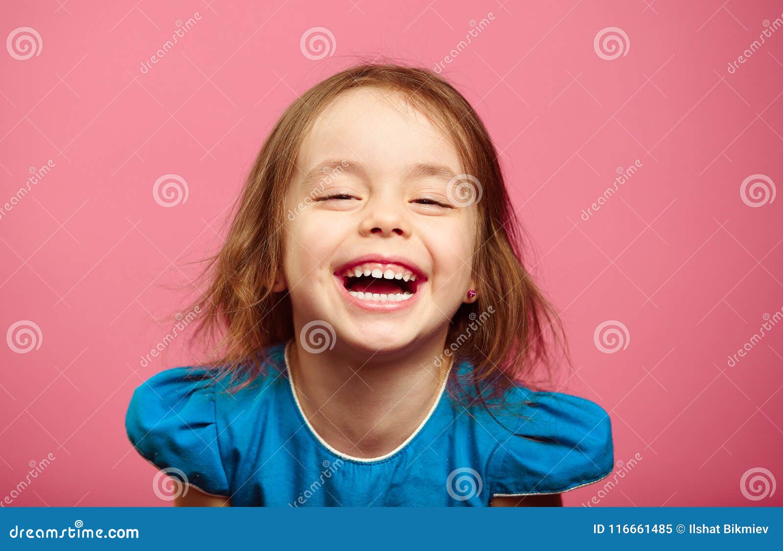 frontal shot of laughter joyful little girl stands beside pink wall.
