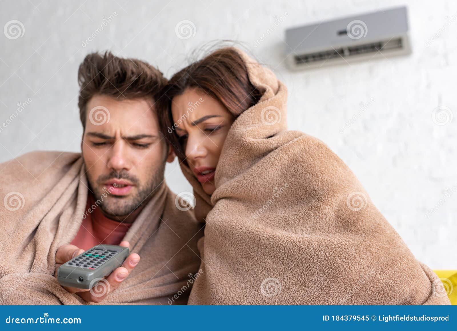 Couple Warming Under Blankets while Sitting Under Air Conditioner with