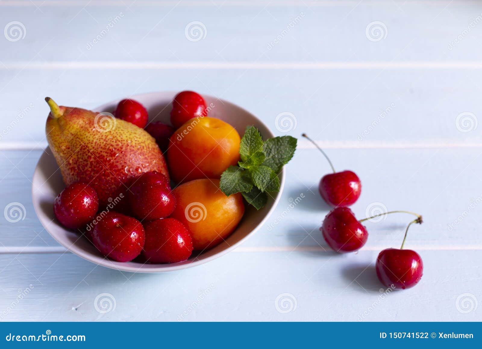 Fruit in a bowl. Red cherry, apricots, Forelle pear with fresh mint in a white bowl.