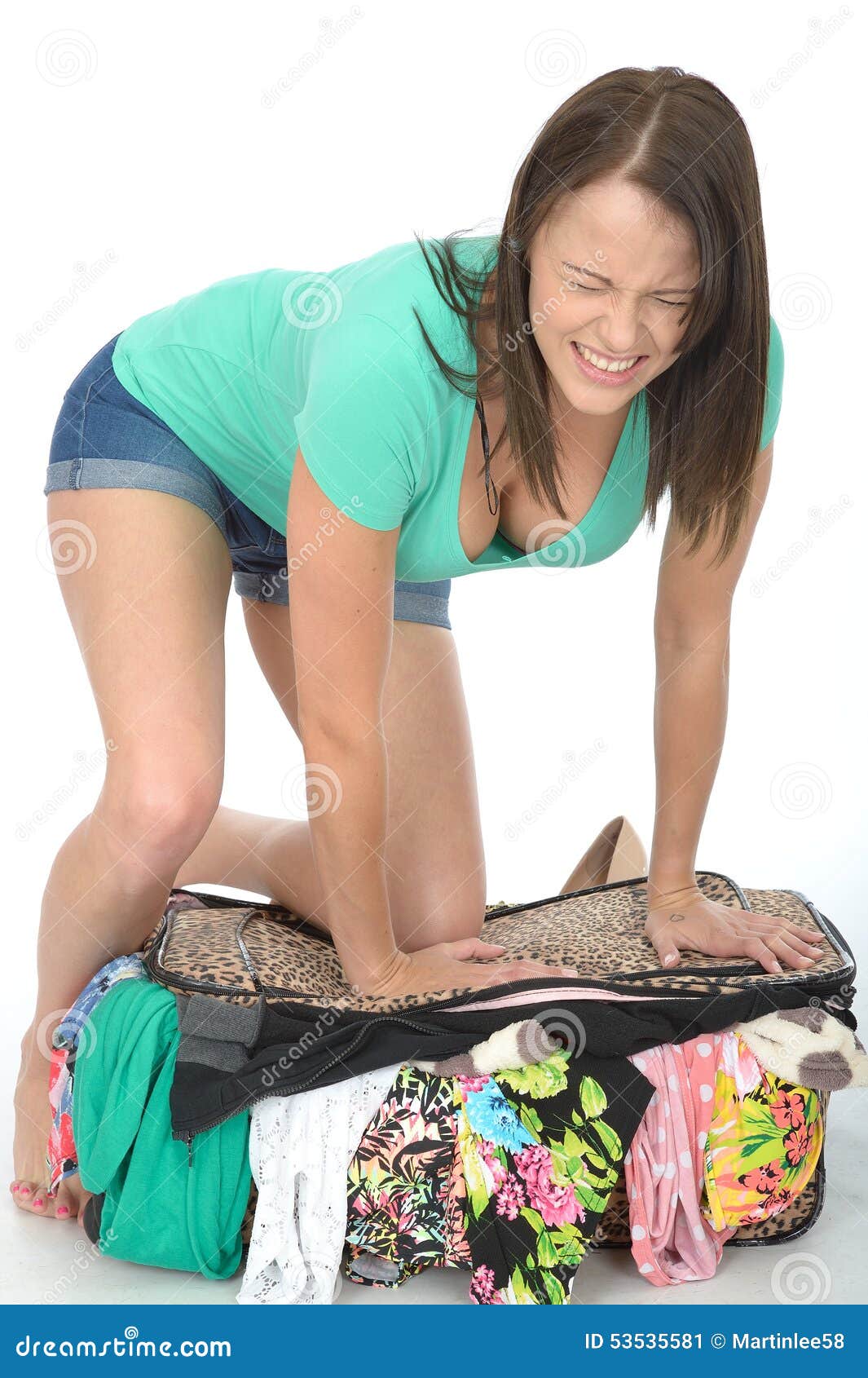 frustrated stressed angry young woman trying to close an overflowing suitcase