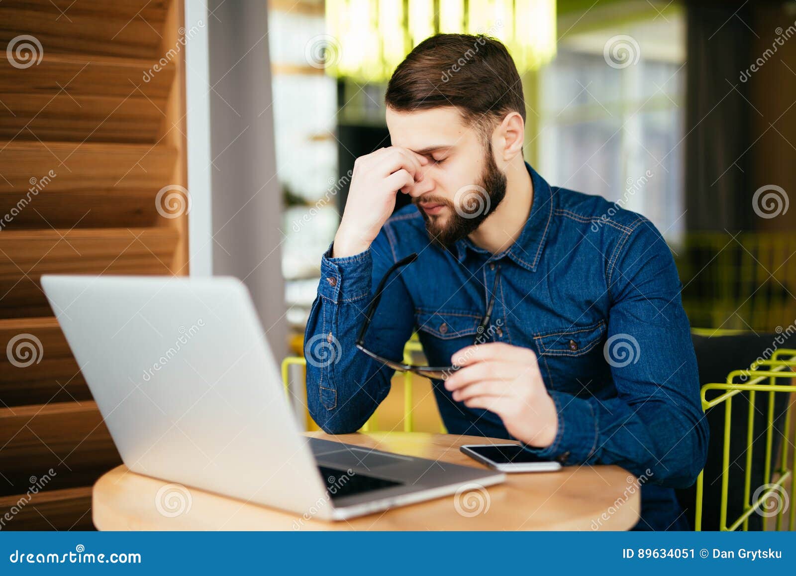 Feeling exhausted. Frustrated young beard man massaging his nose and keeping eyes closed while sitting at his working place in office