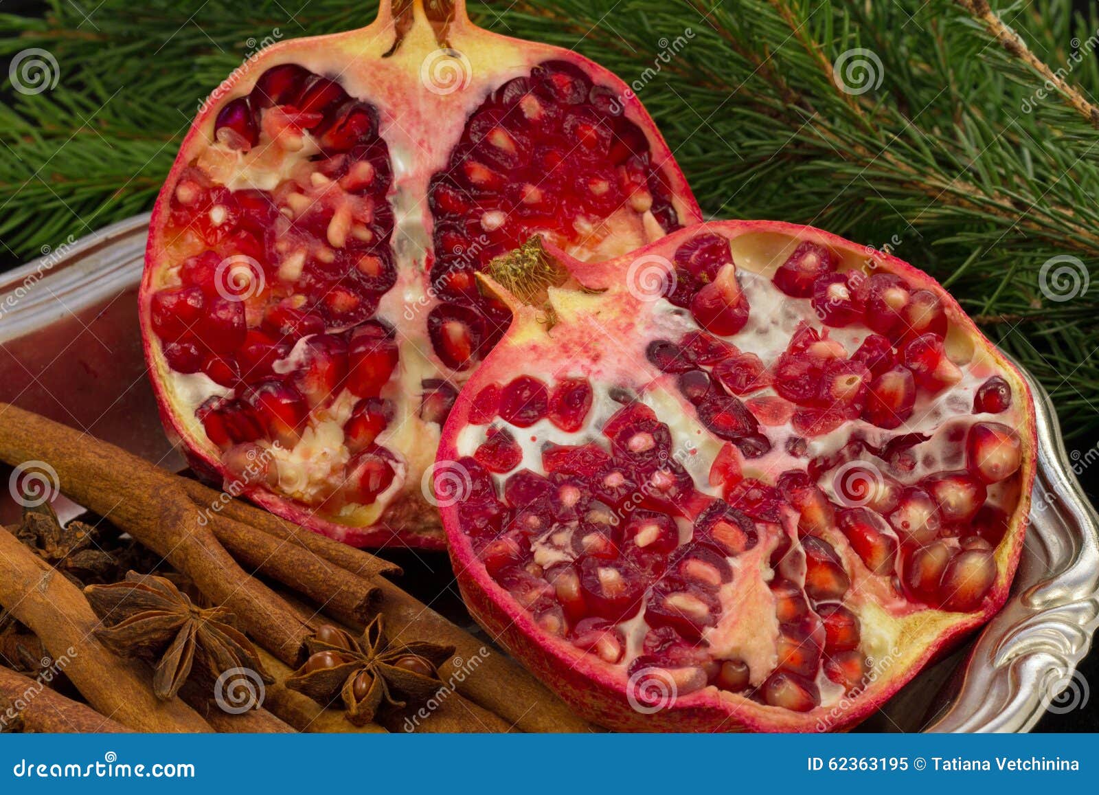 Fruta roja de la granada en fondo negro en una placa y un canela y una rama del árbol de navidad