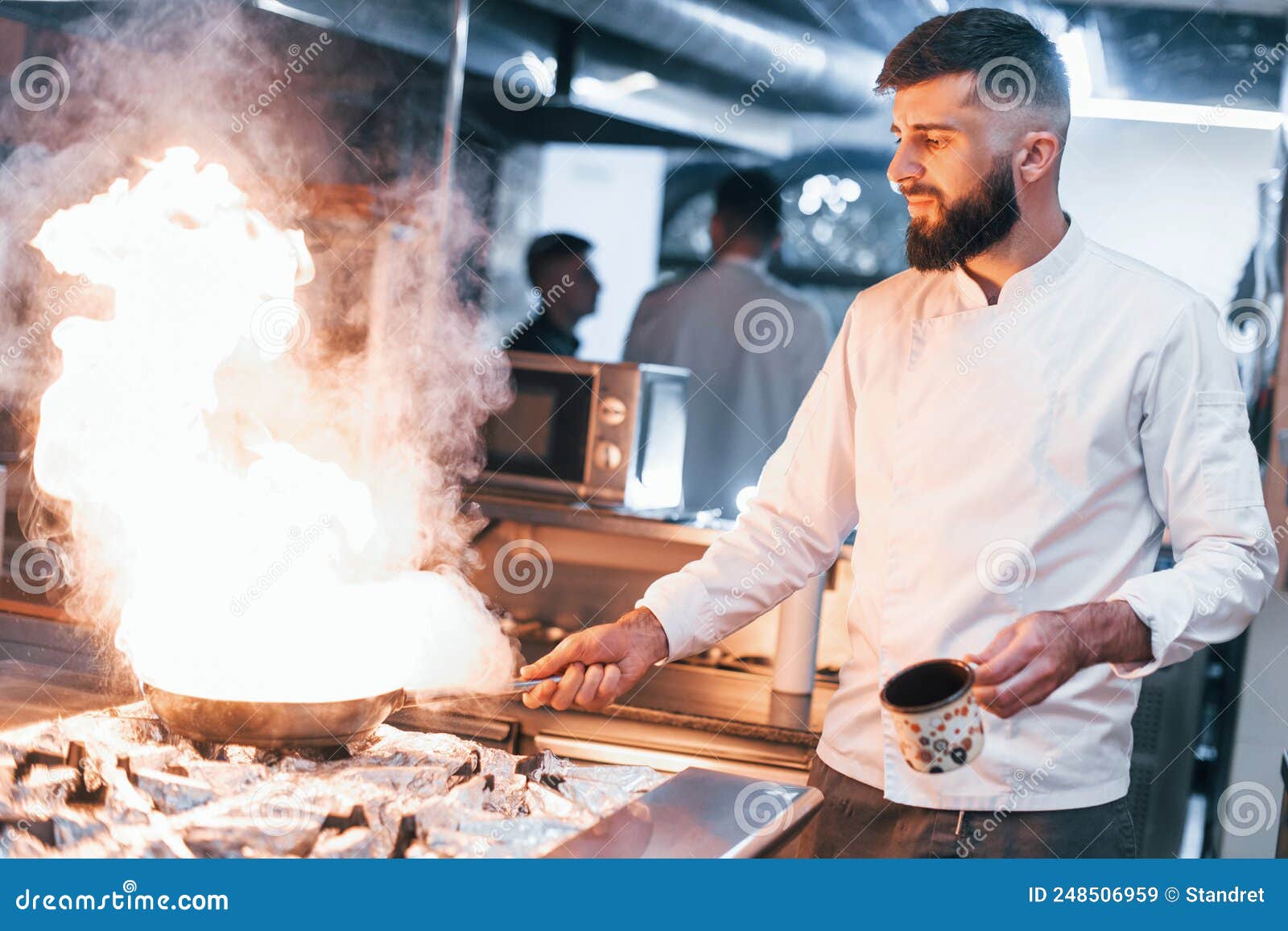 Frying Pan is on Fire. Chef in White Uniform Cooking Food at Kitchen