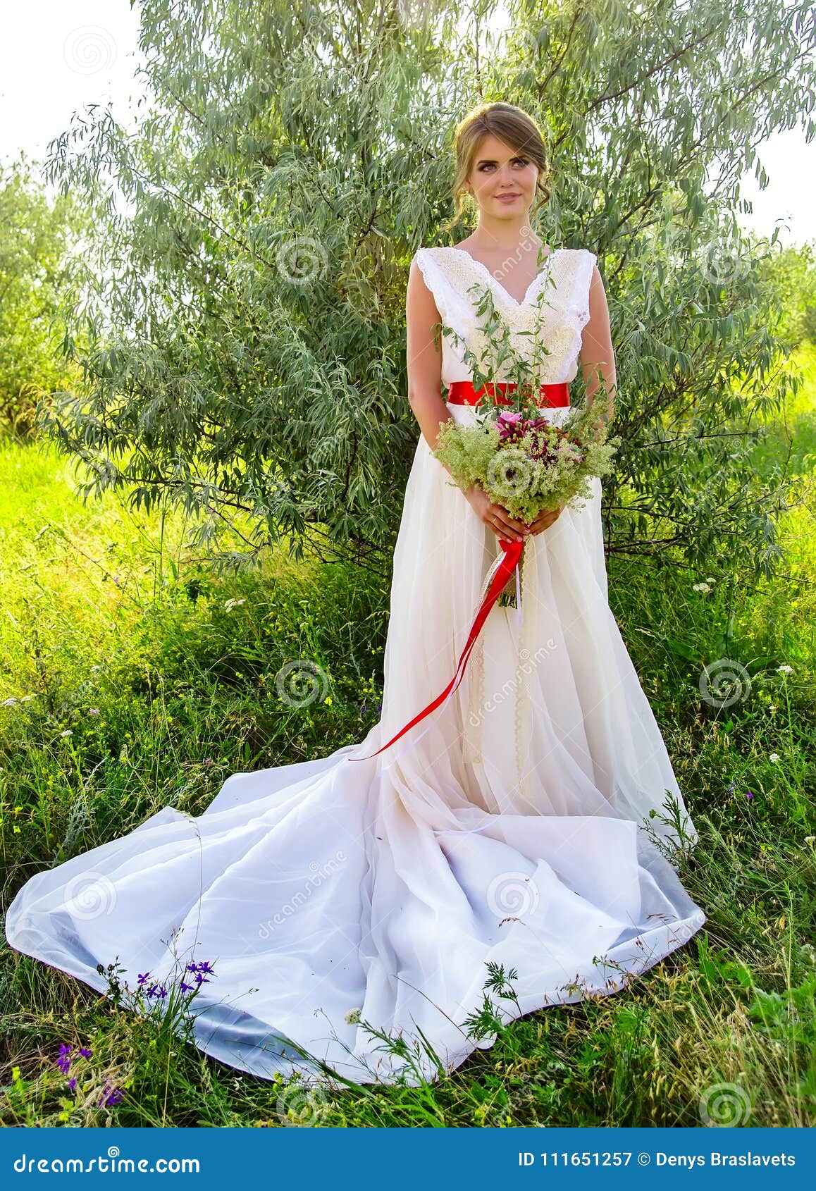 Bride With A Bouquet In A White Dress With A Red Ribbon Near A