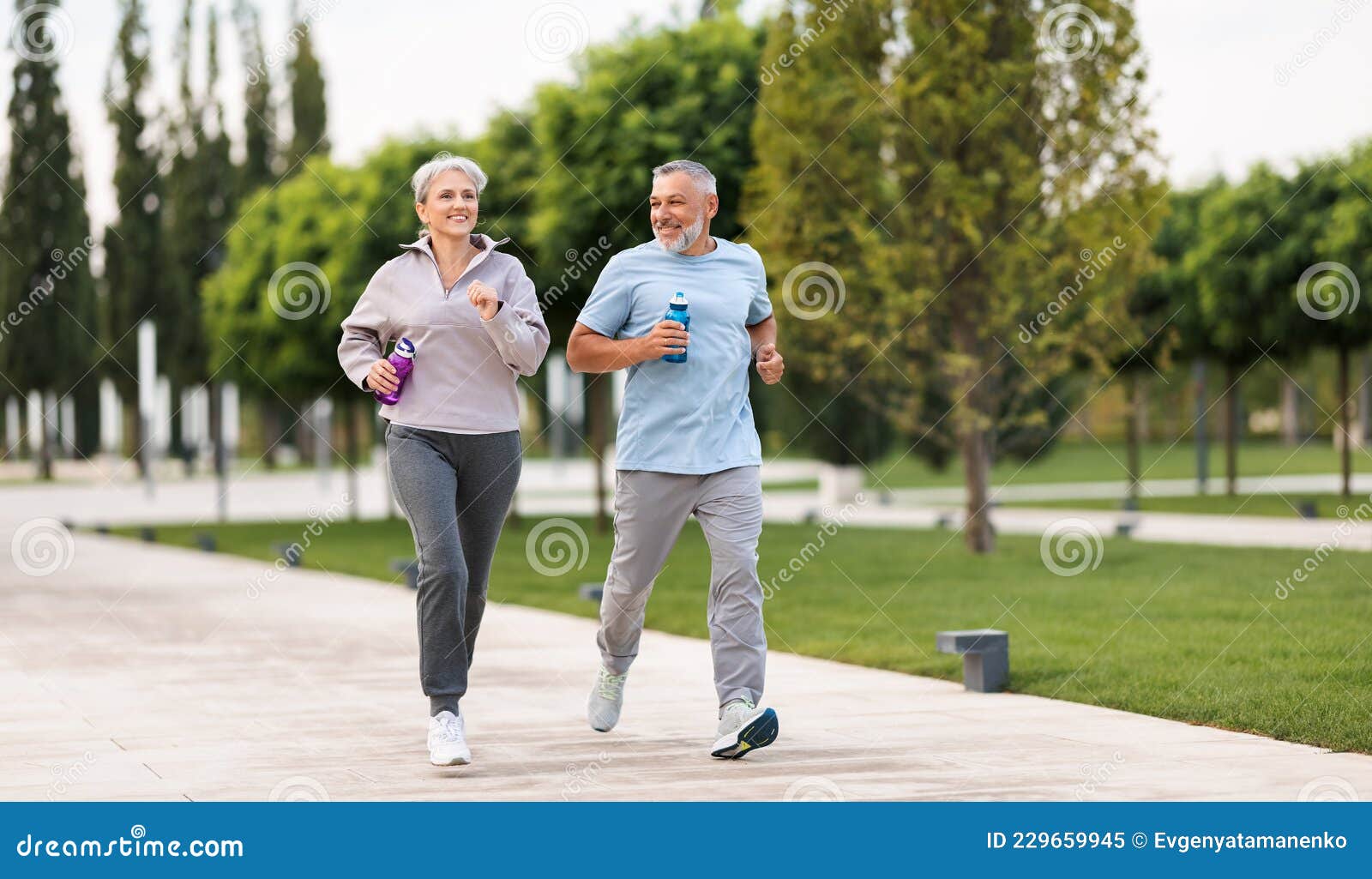 full-length photo of lovely joyful retirees couple jogging outside in city park