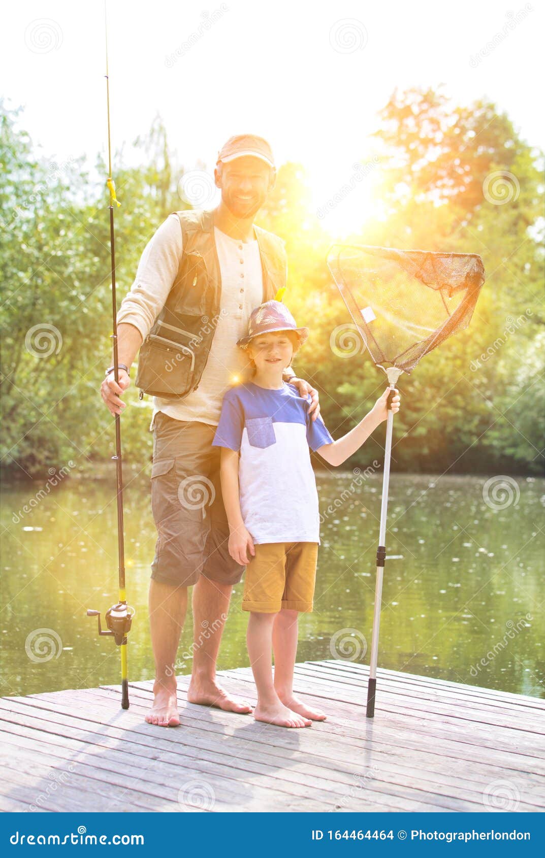 full length portrait of smiling father and son  standing with fishing  tackles on pier against lake