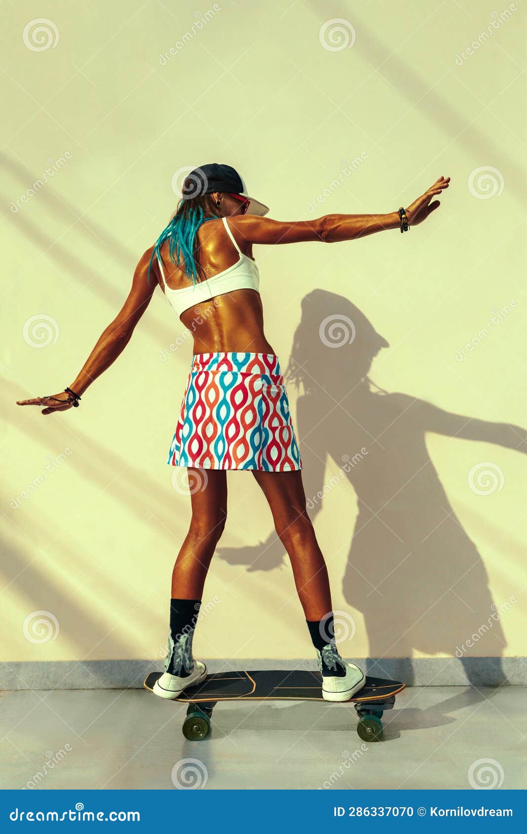 full-length shot of a skater woman`s back wearing fancy clothes and riding her skateboard in front of a yellow wall with shadows