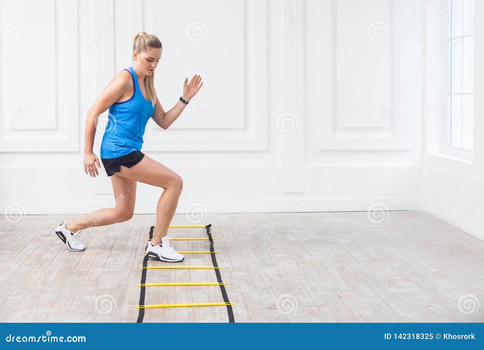 full length of sporty beautiful young athletic blonde woman in black shorts and blue top are hard working and training on agility
