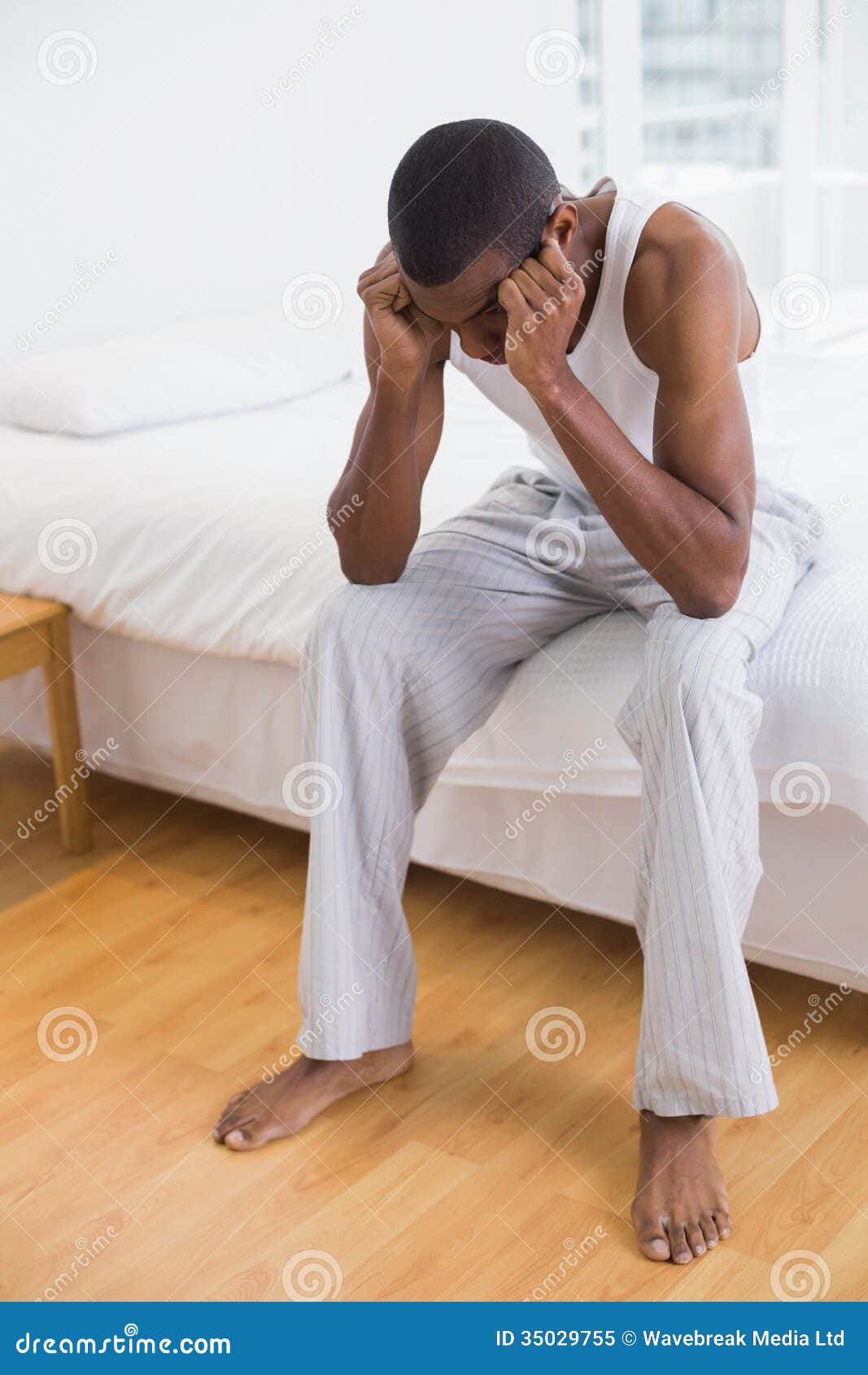 Full Length of a Thoughtful Young Afro Man Sitting on Bed Stock Image