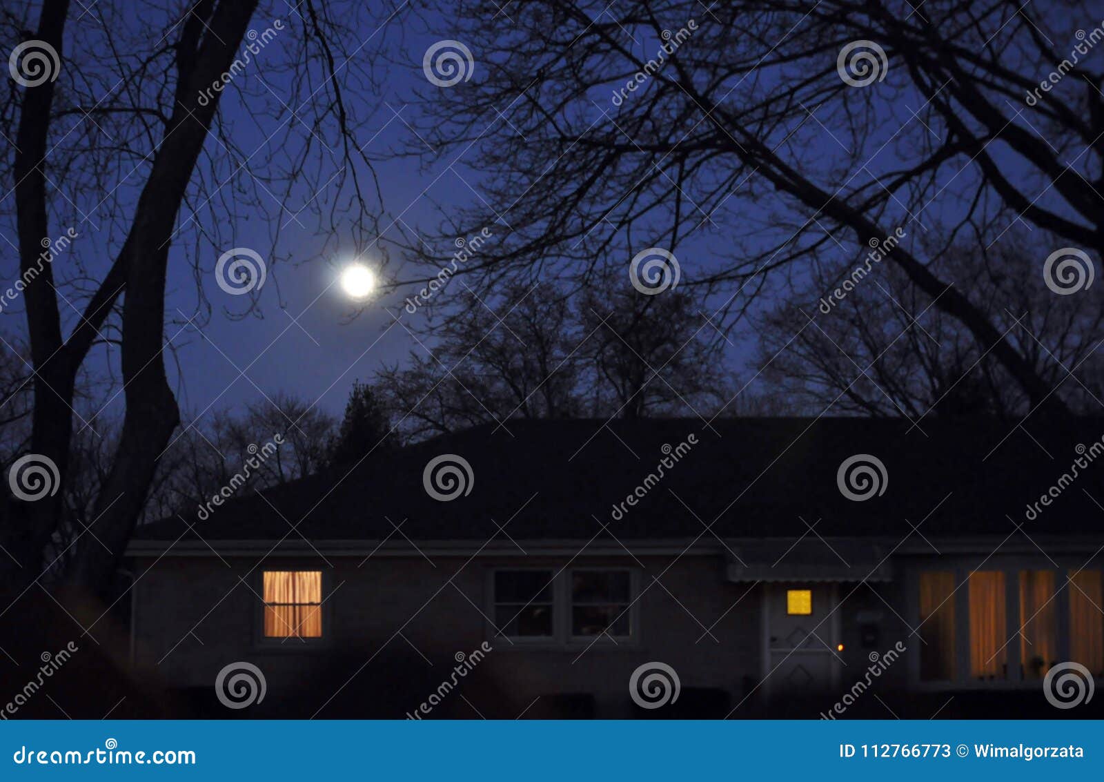 moon rise over a house with lights on.