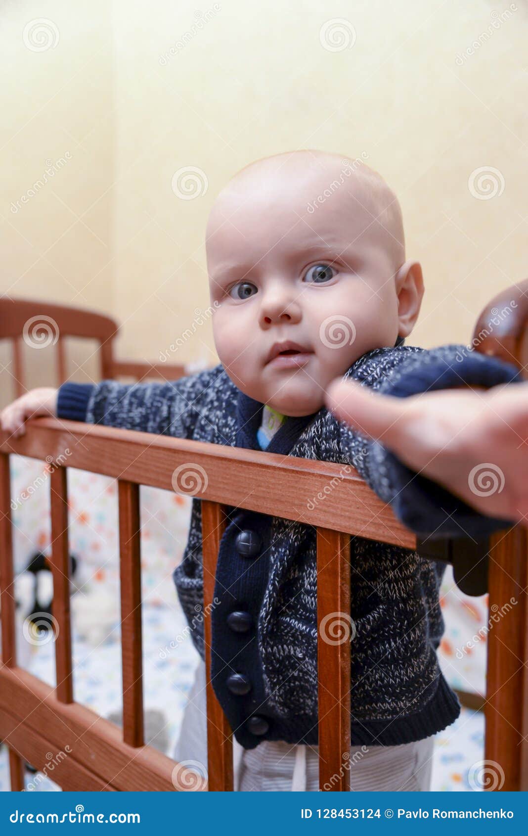 Funny Baby Standing in a Crib and Pulls a Hand Forward Stock Photo