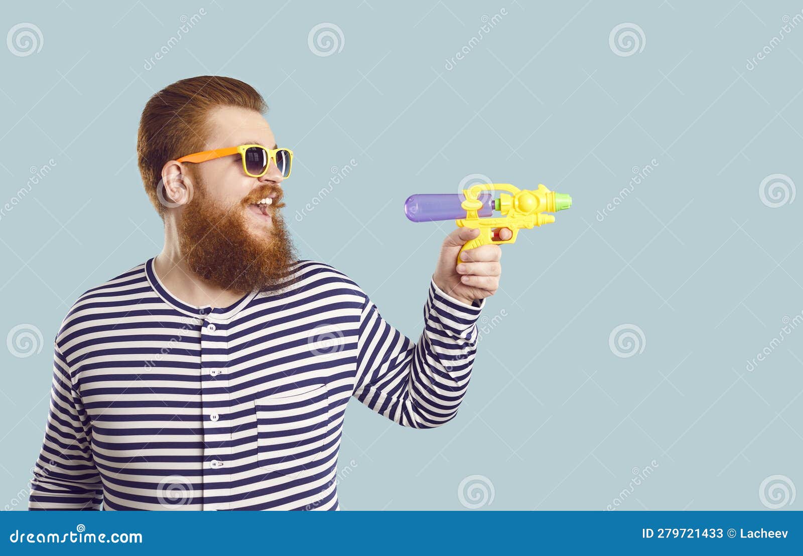 funny bearded chubby male tourist shoots with small water pistol towards copy space.