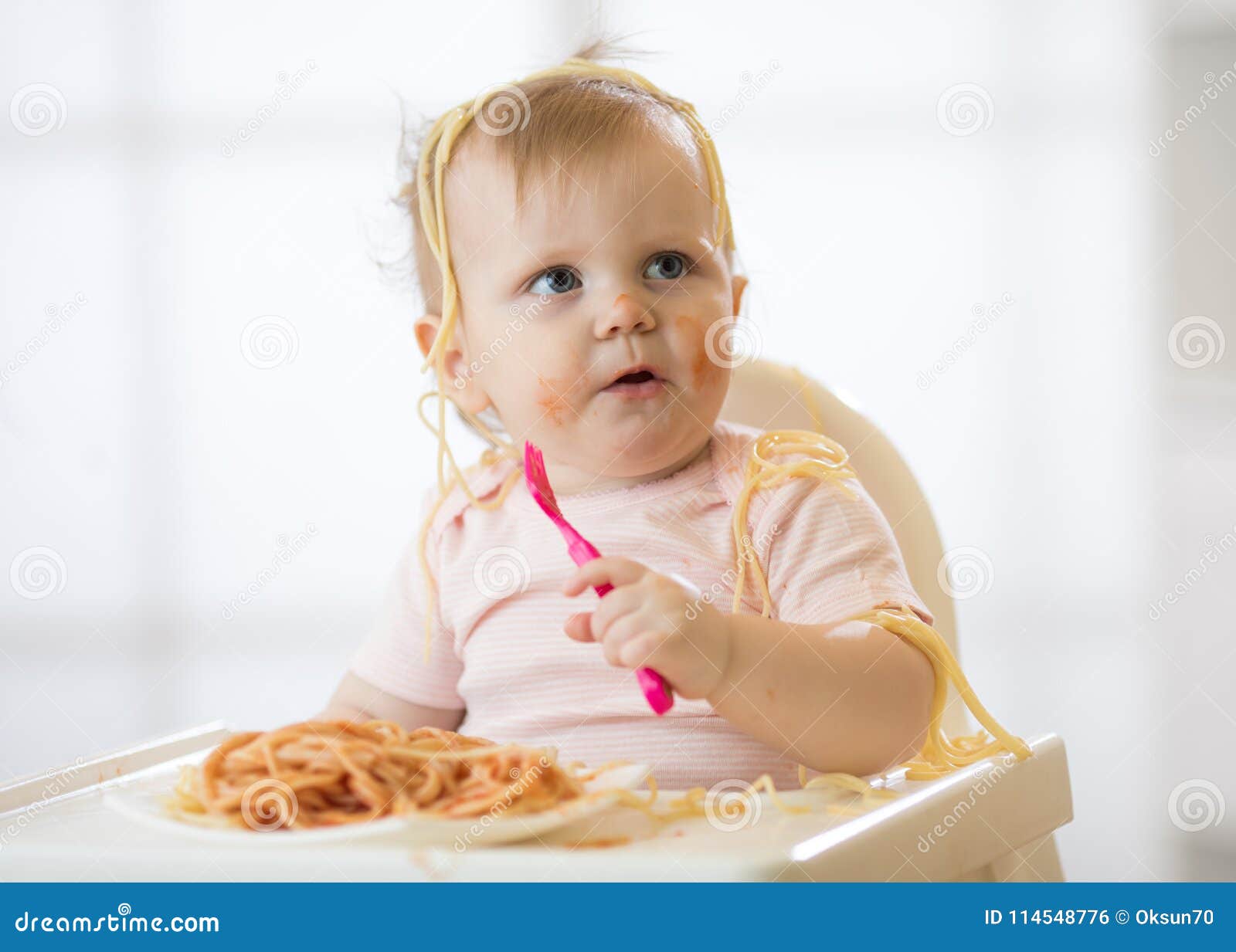 funny child eating noodle. grimy kid eats spaghetti with fork sitting on table at home