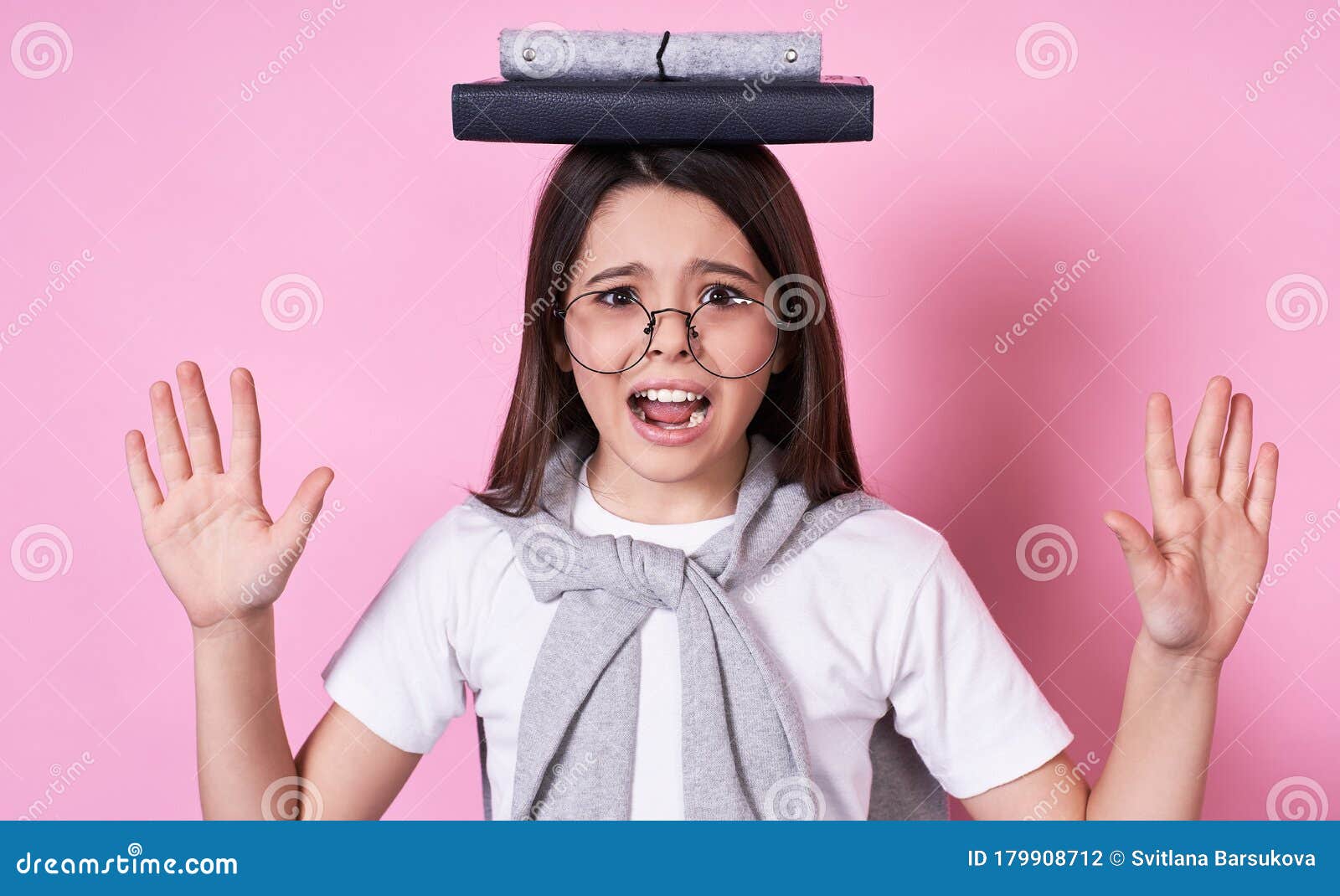 Cute Young Funny Schoolgirl In Glasses Holds Books On Her Head On A