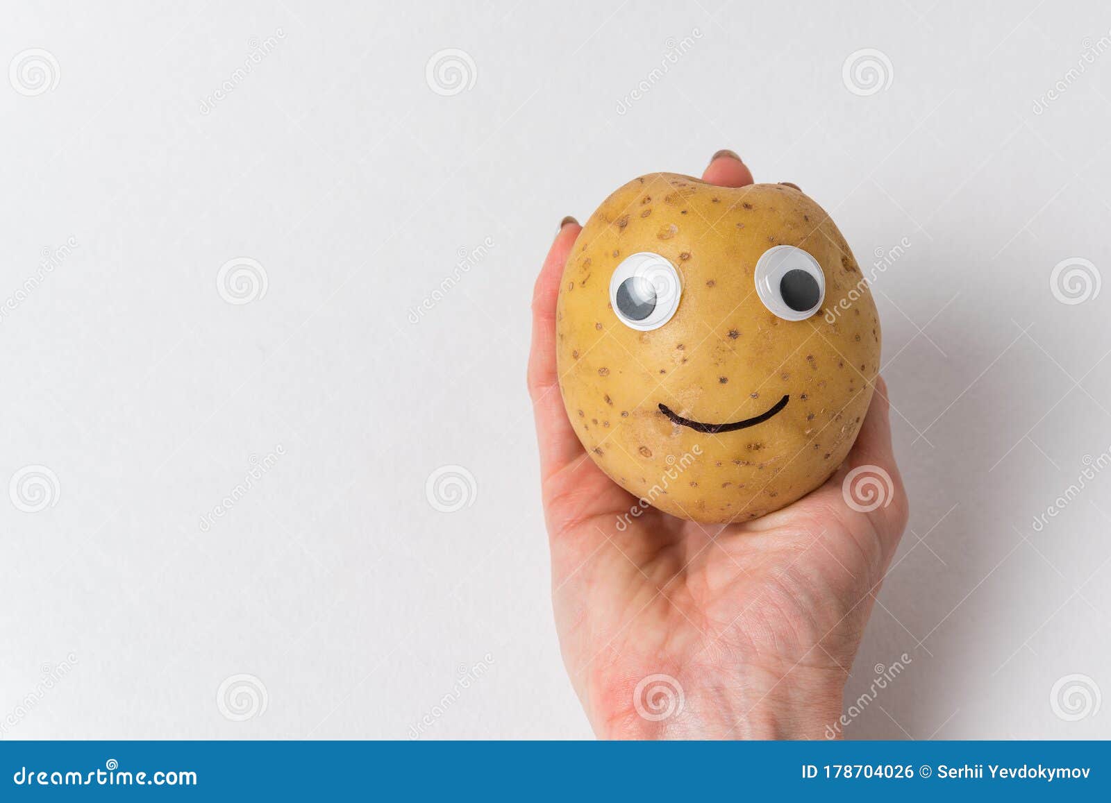 Funny Potato with Eyes and Painted Smile is on the Hand on White