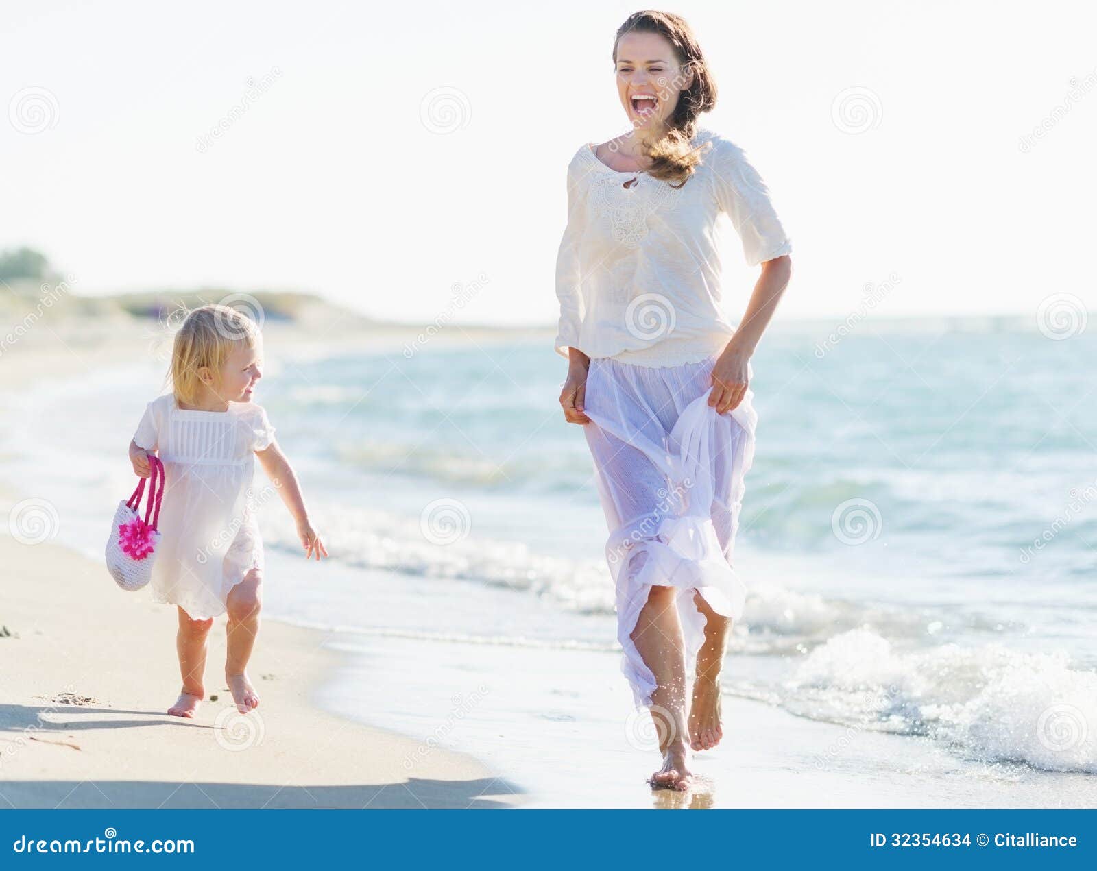 Funzionamento felice del bambino e della madre sulla riva di mare. Giovane funzionamento felice della neonata e della madre sulla riva di mare