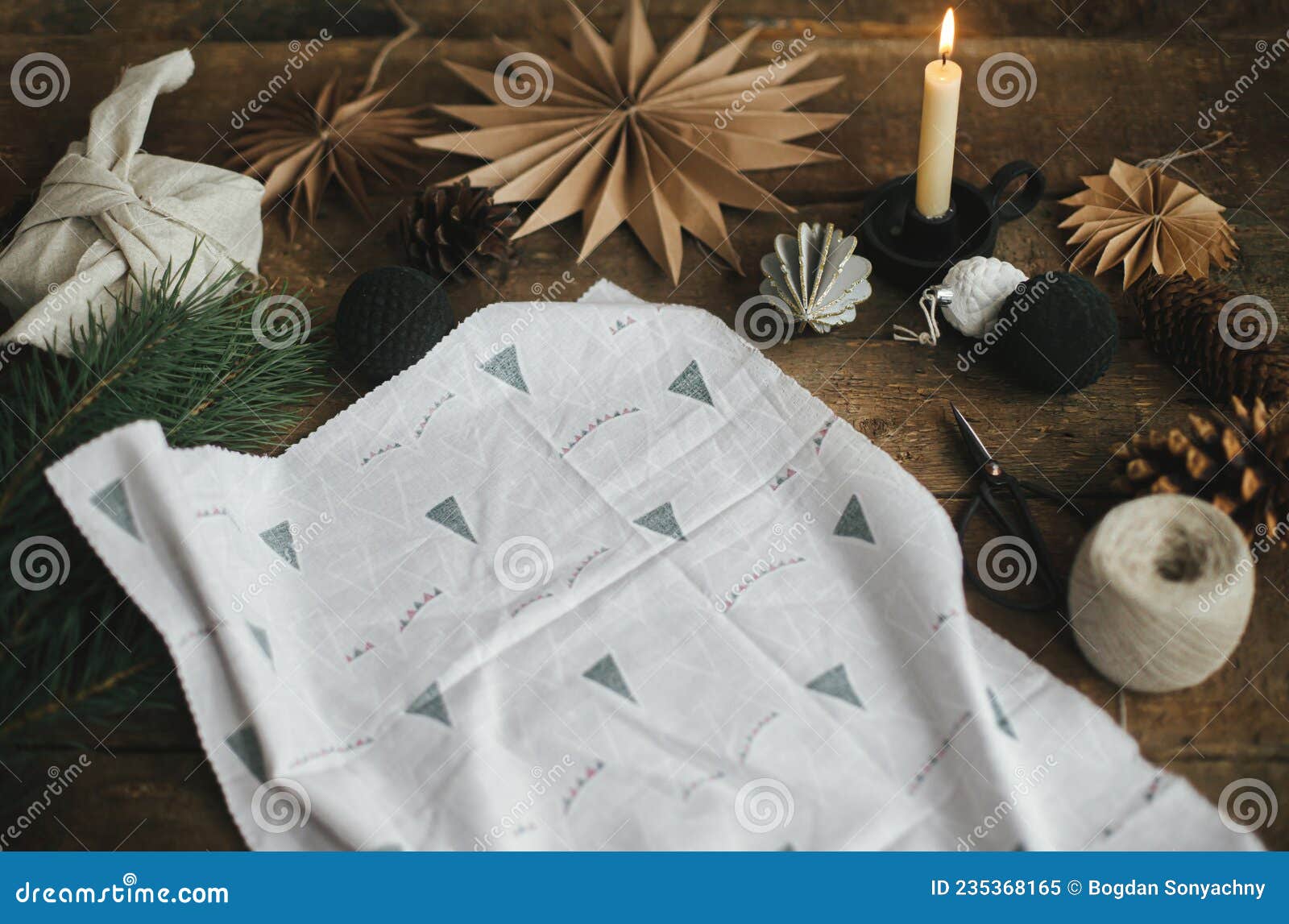 Stylish christmas gift wrapped in fabric on rustic table with scissors,  paper star, candle.Furoshiki Stock Photo by Sonyachny