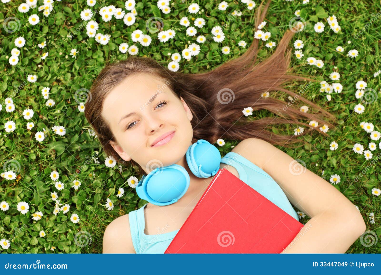 Fêmea nova com o livro e os auscultadores que encontram-se em uma grama com fluxo. A fêmea nova com livro e os auscultadores que encontram-se em uma grama com margarida florescem