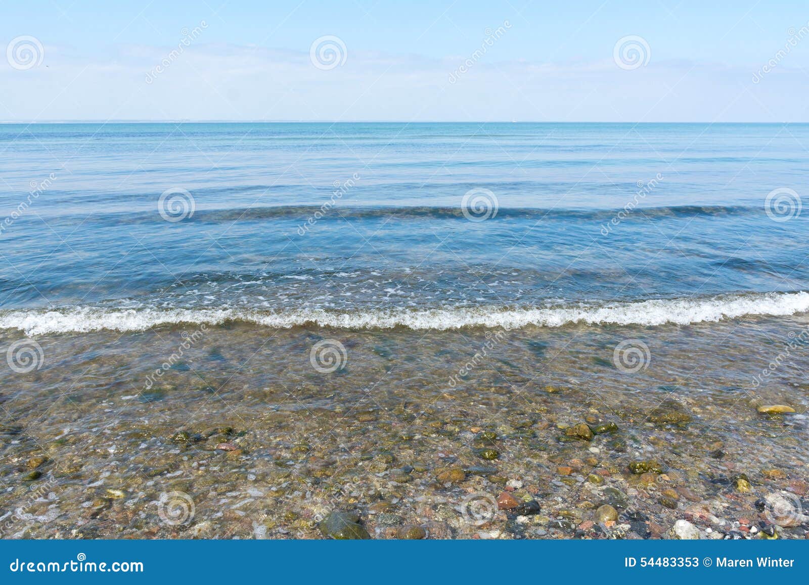 Försiktig havsbränning på en strand av kiselstenar, horisont och blå himmel, för. Försiktig havsbränning på en strand av kiselstenar på kusten av Östersjön, horisonten och den blåa himlen som är frontal