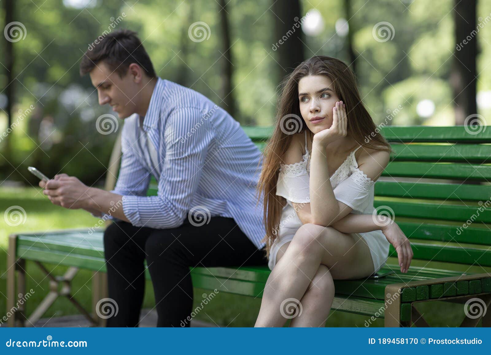 gadget addiction. bored young girl and her boyfriend stuck in cellphone on dull date at park