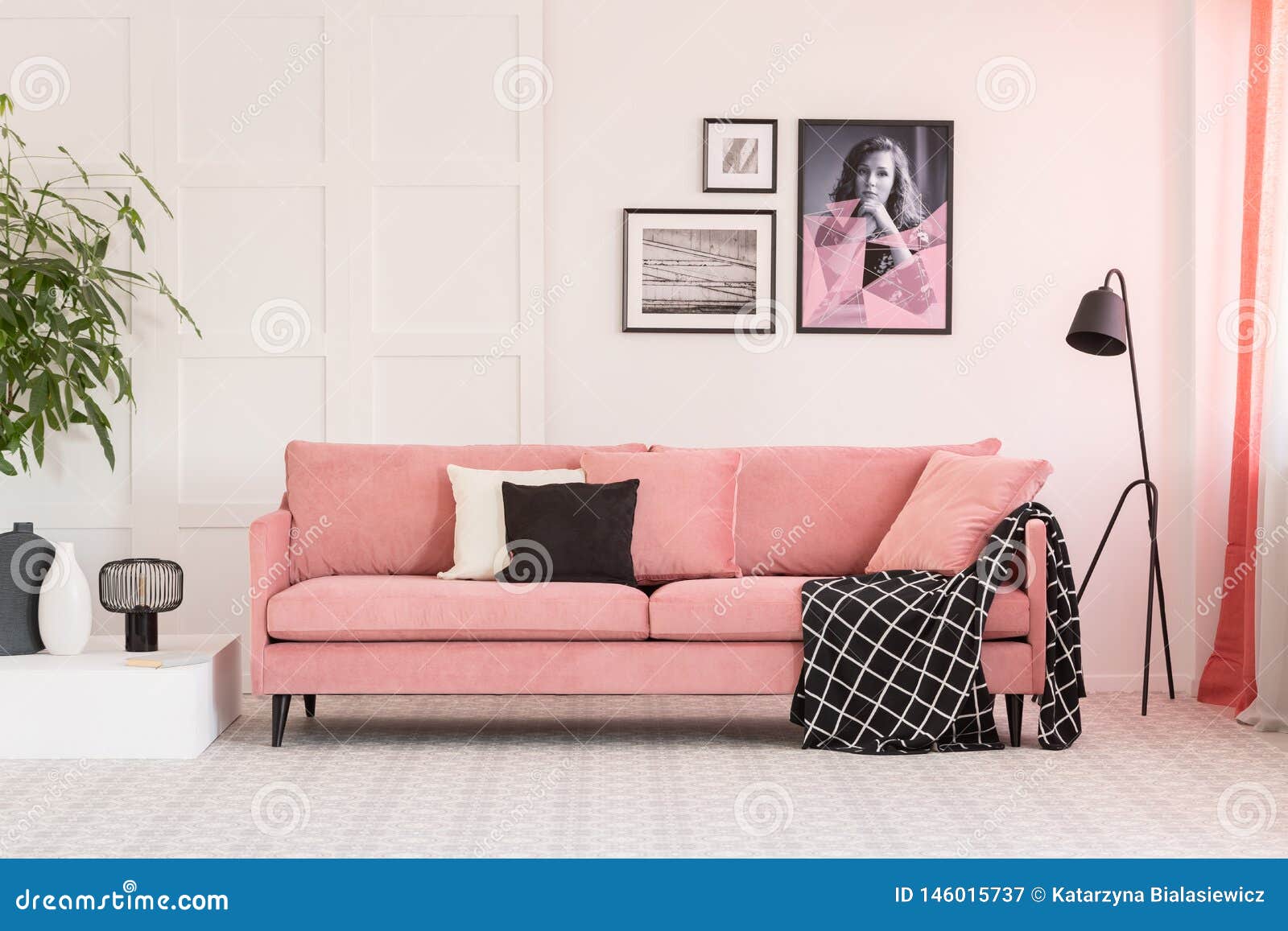 gallery of posters on wall in fashionable living room interior with pink couch and industrial lamp