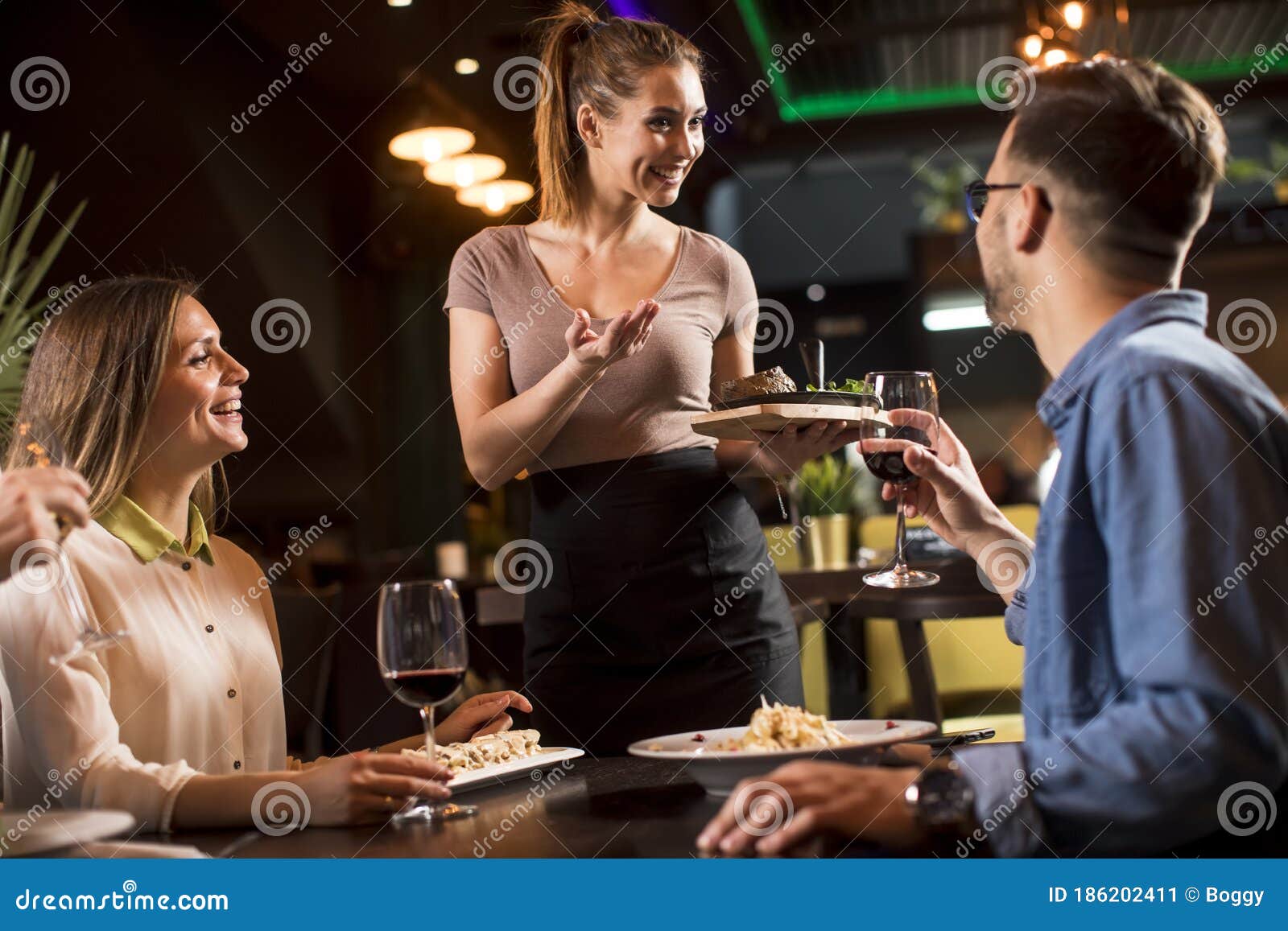 Garçonete bonita servindo grupo de amigas com comida no restaurante