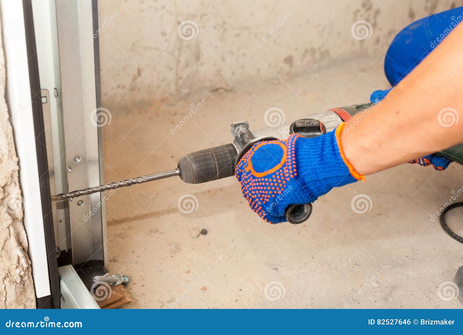Garage Doors Installation. Worker Drills a Hole for the Bolt. Stock