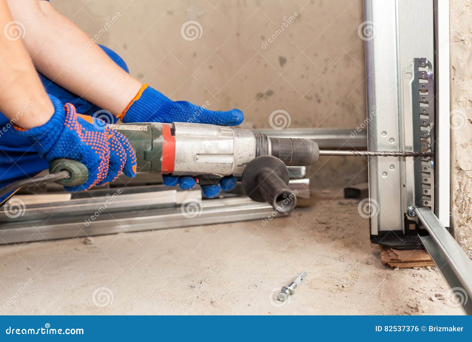 Garage Doors Installation. Worker Drills a Hole for the Bolt. Stock