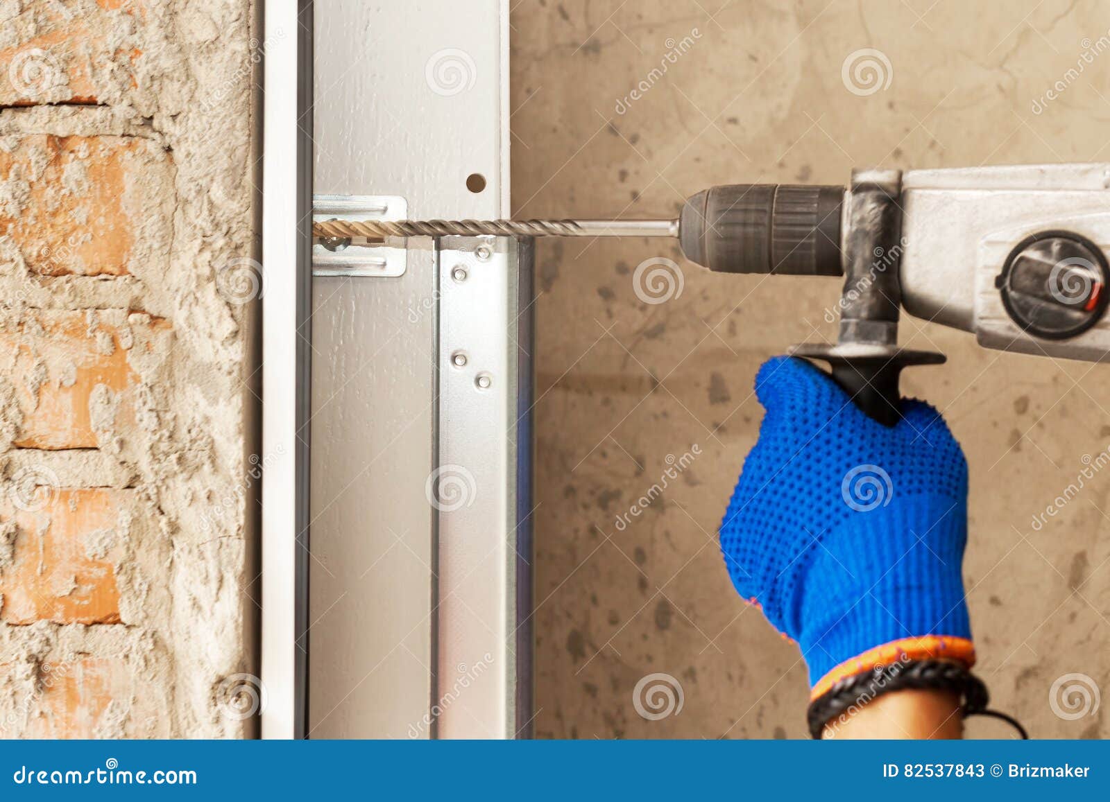 Garage Doors Installation. Worker Drills a Hole for the Bolt. Stock