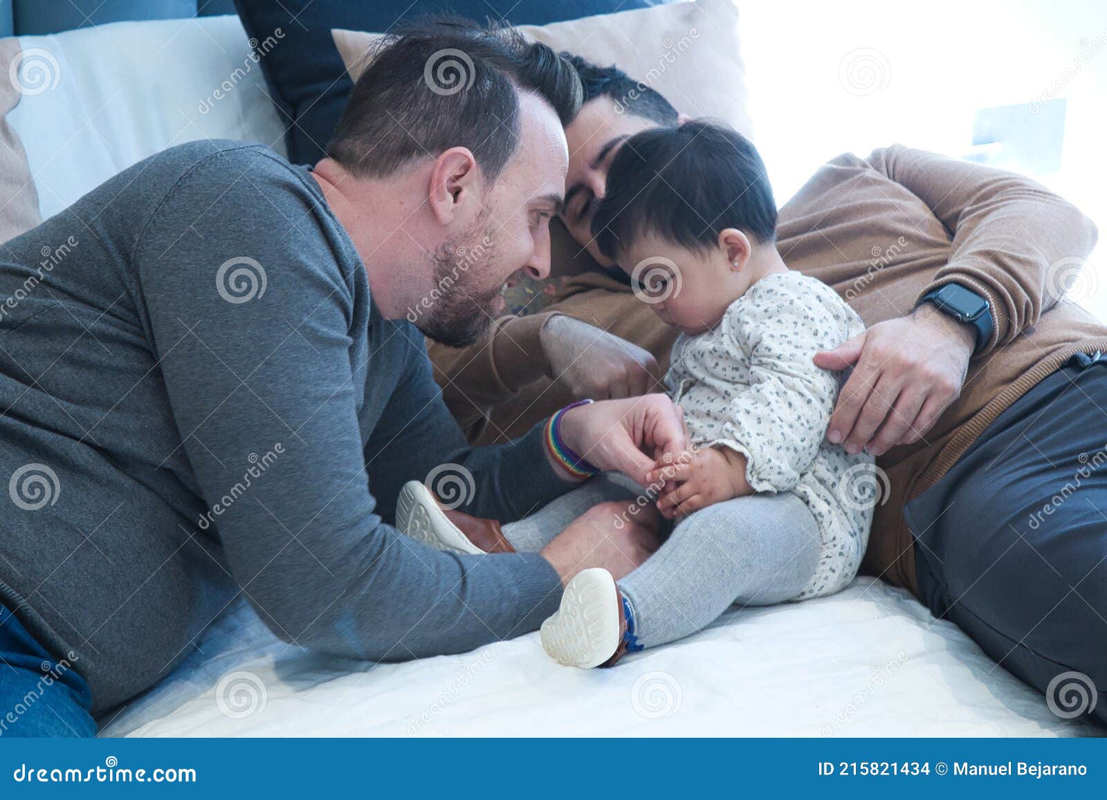 Gay Couple Playing with Their Daughter on the Marriage Bed in Their Home Stock Photo