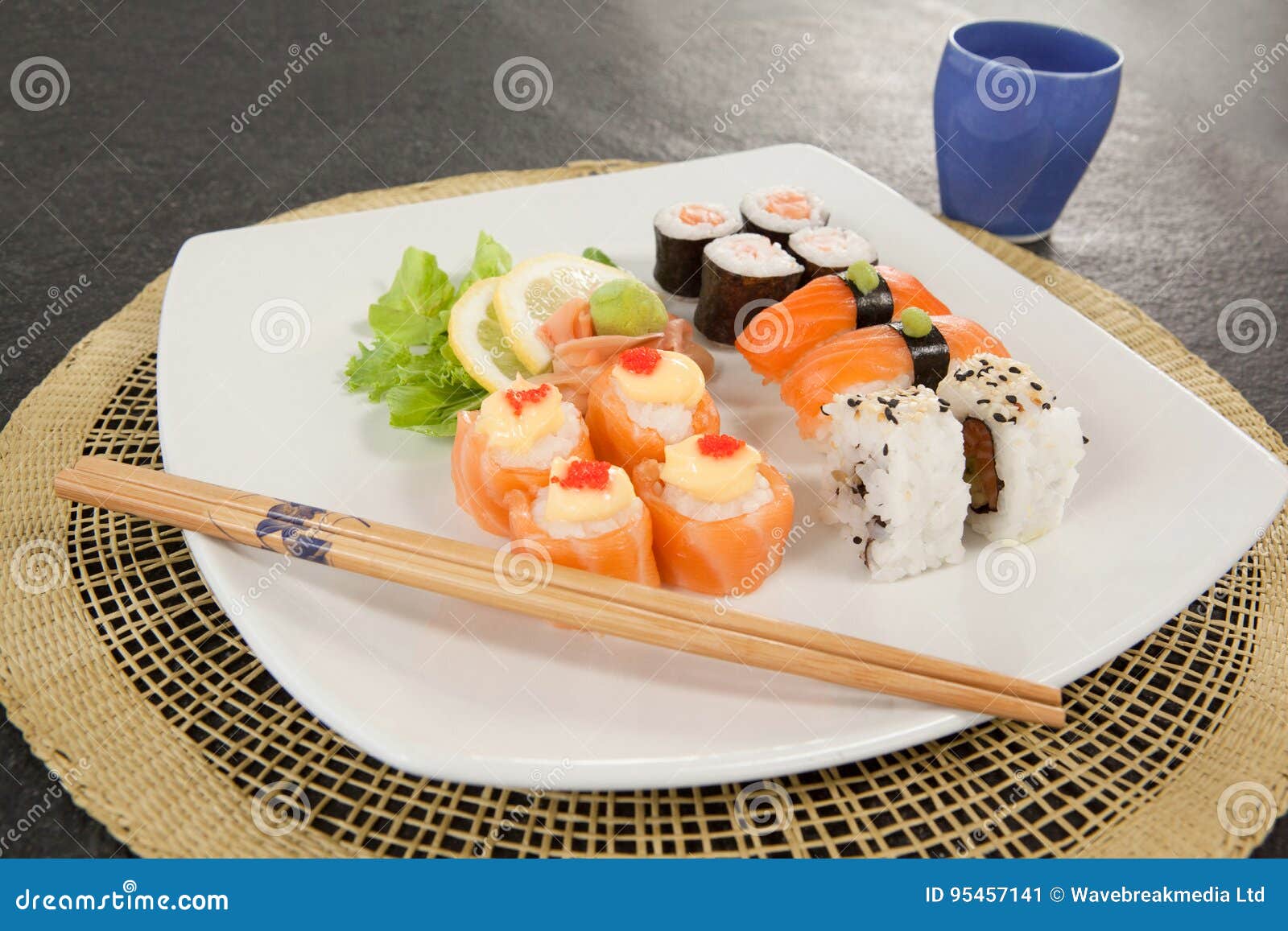 Geassorteerde die sushireeks met eetstokjes en glas op sushimat wordt gediend. De geassorteerde sushireeks diende met eetstokjes en glas op sushimat tegen zwarte achtergrond