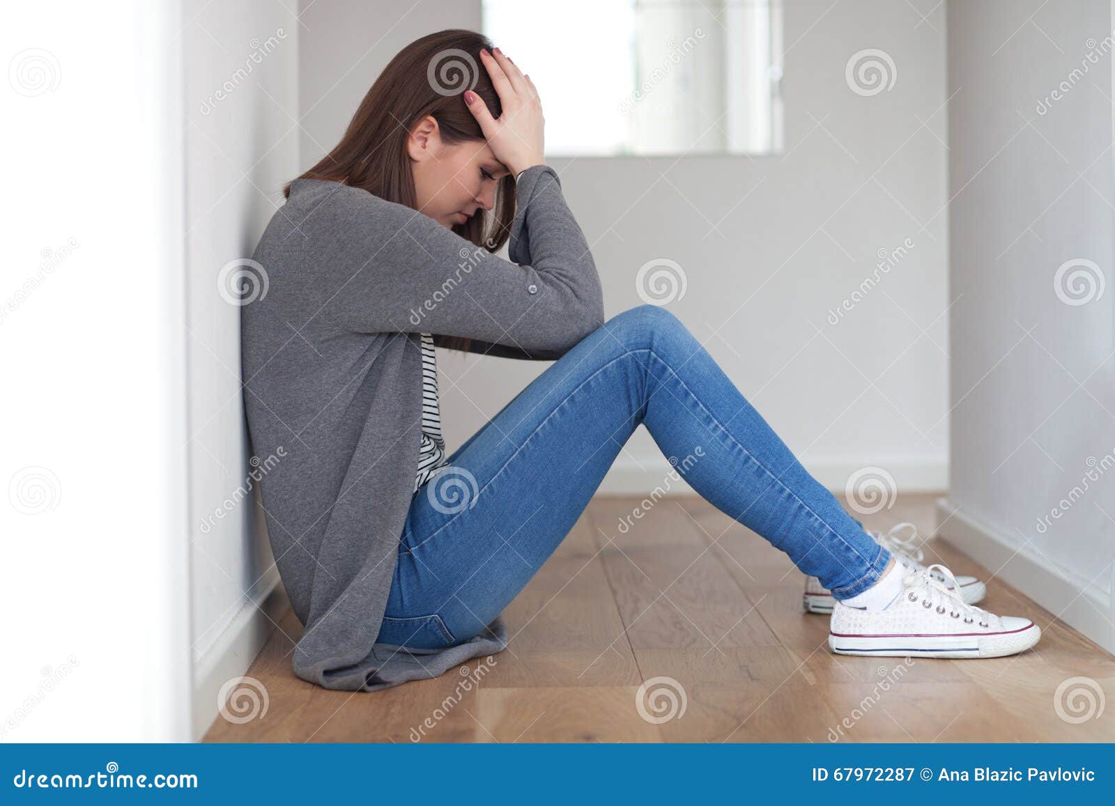 Gedeprimeerde jonge vrouw. Het droevige kijken jonge vrouwenzitting op vloer, op witte achtergrond
