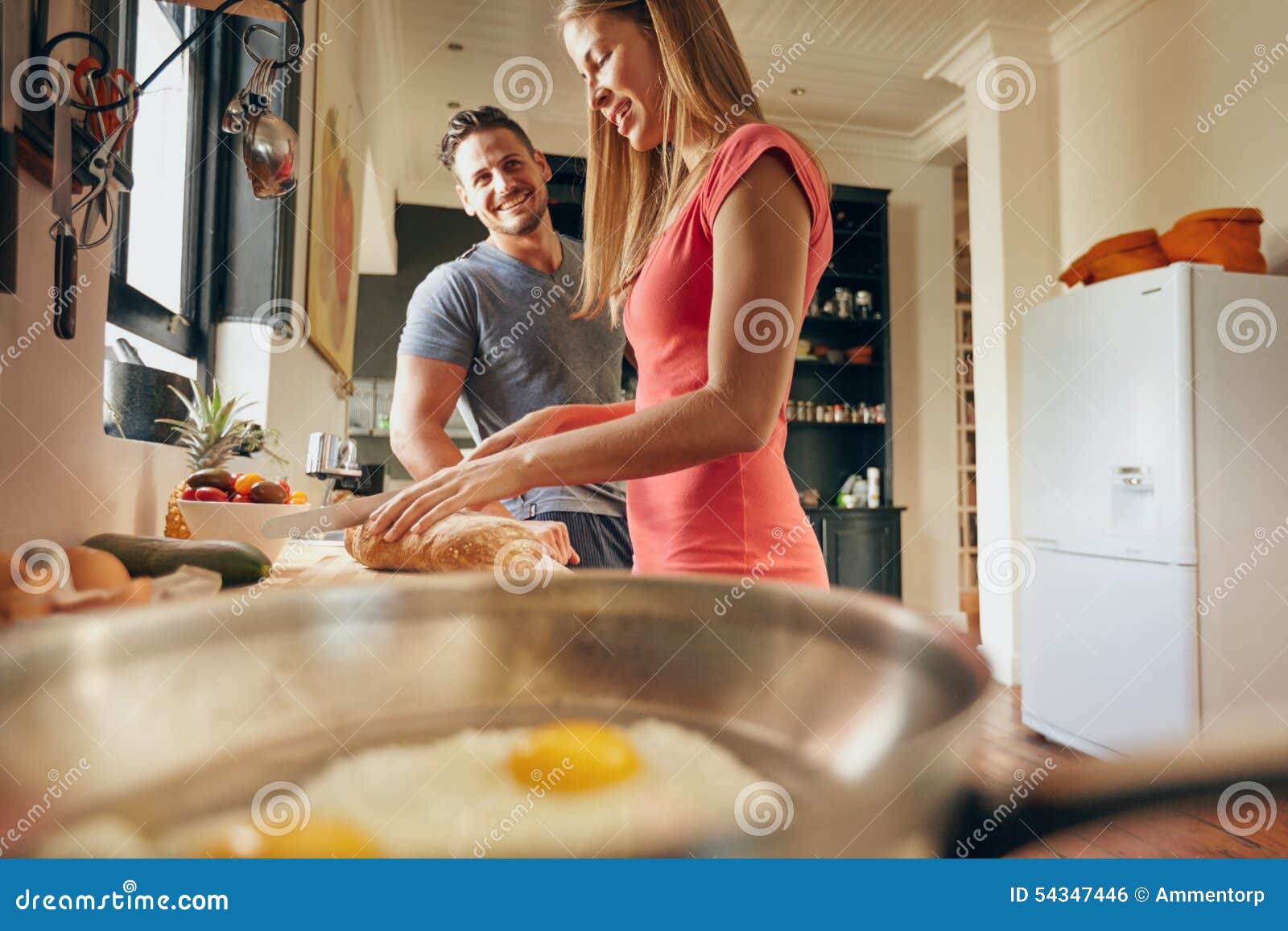 Gelukkig paar in keuken. Binnenschot van gelukkig jong paar die zich bij de keukenteller bevinden in ochtend Vrouwen scherp brood voor ontbijtnadruk op jonge vrouwen die voedsel voorbereiden terwijl mannen die bij haar glimlachen