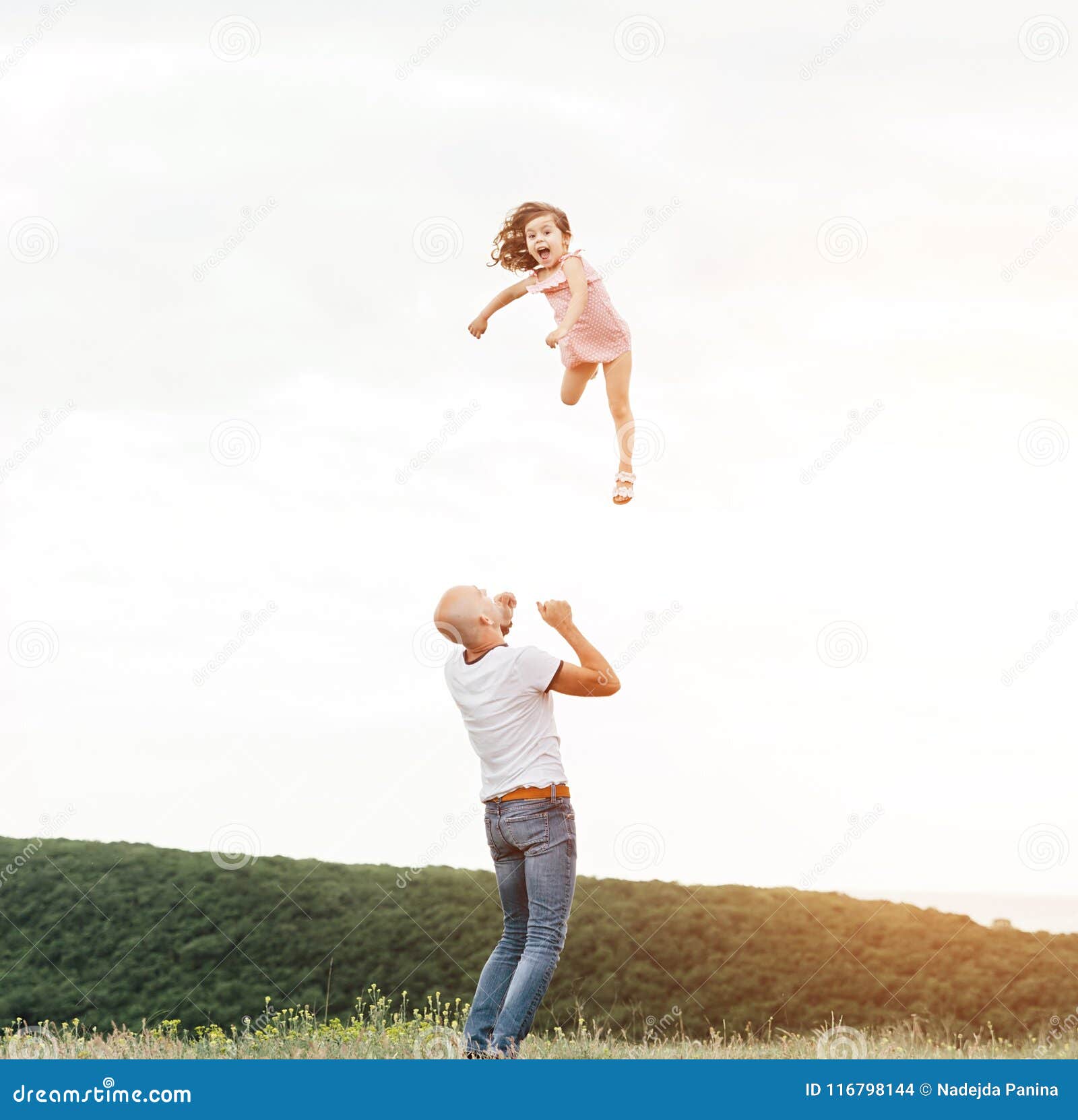 Generi il gioco con sua figlia nel campo soleggiato. Padre felice che gioca con sua figlia nel campo soleggiato sul tramonto Stile di vita felice della famiglia di estate, vero emozioni Bambina che vola su nel cielo dalle mani del ` s del papà