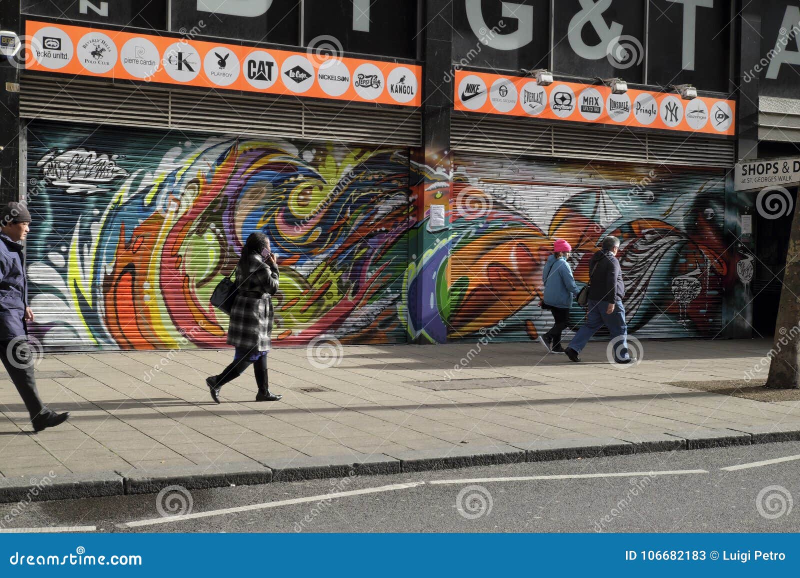 Gente que camina más allá de pintada en Croydon, Reino Unido. Gente que camina más allá de dos tiendas cerradas-abajo cuyos obturadores ahora se cubren con la pintada