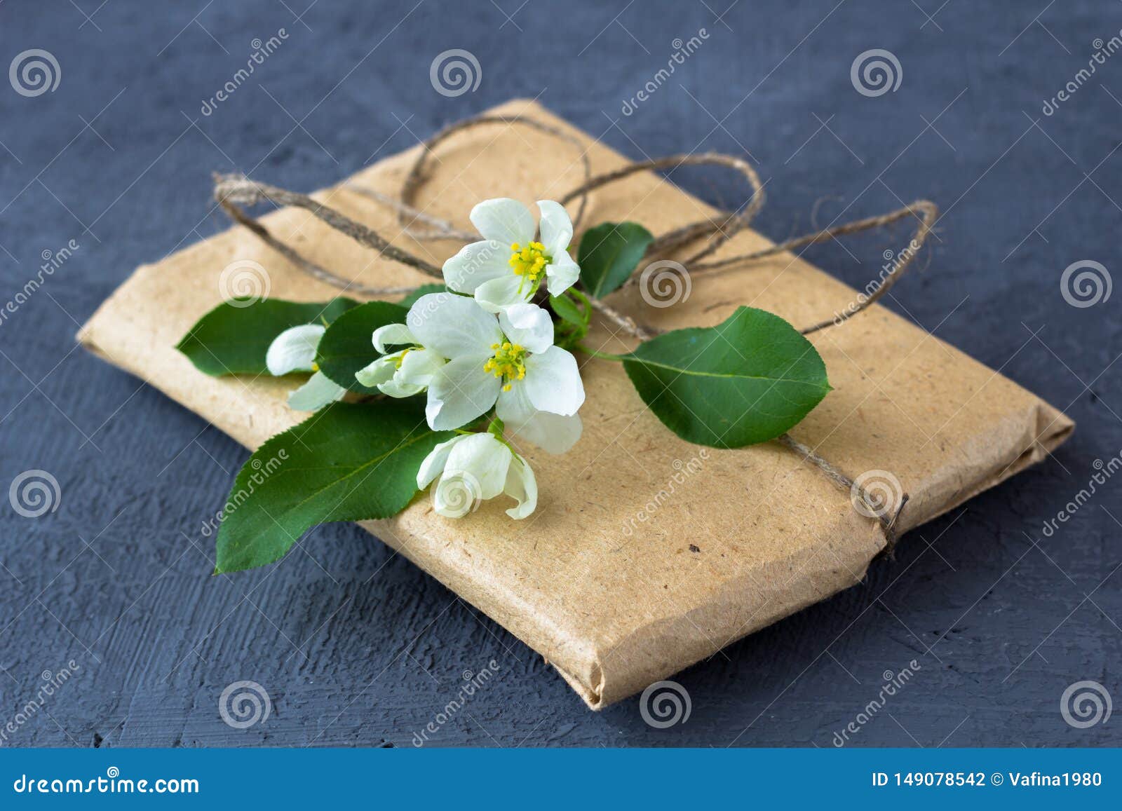 Geschenkkasten eingewickelt im braunen Papier. Geschenkbox eingewickelt im braunen Papier verziert mit Apfelbaumblume auf einem dunklen Hintergrund