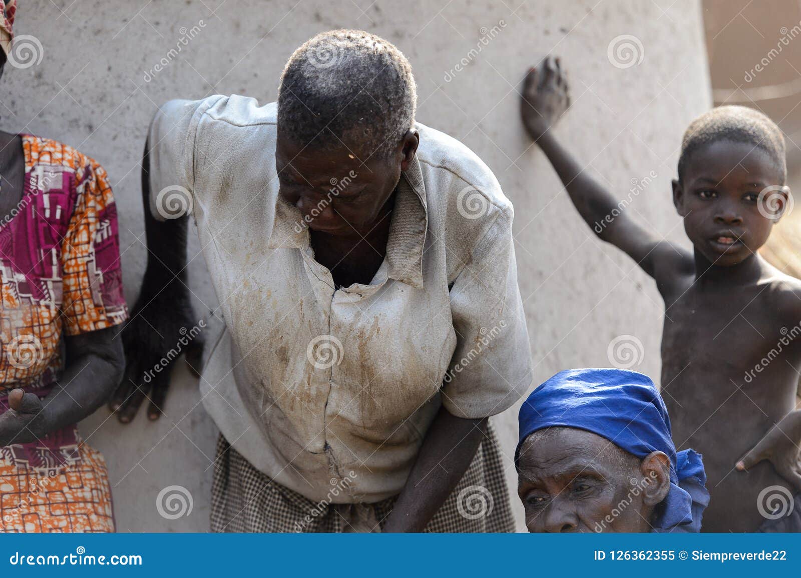 Unidentified Ghanaian Old Man In Dirty Shirt Bends Down Near Th