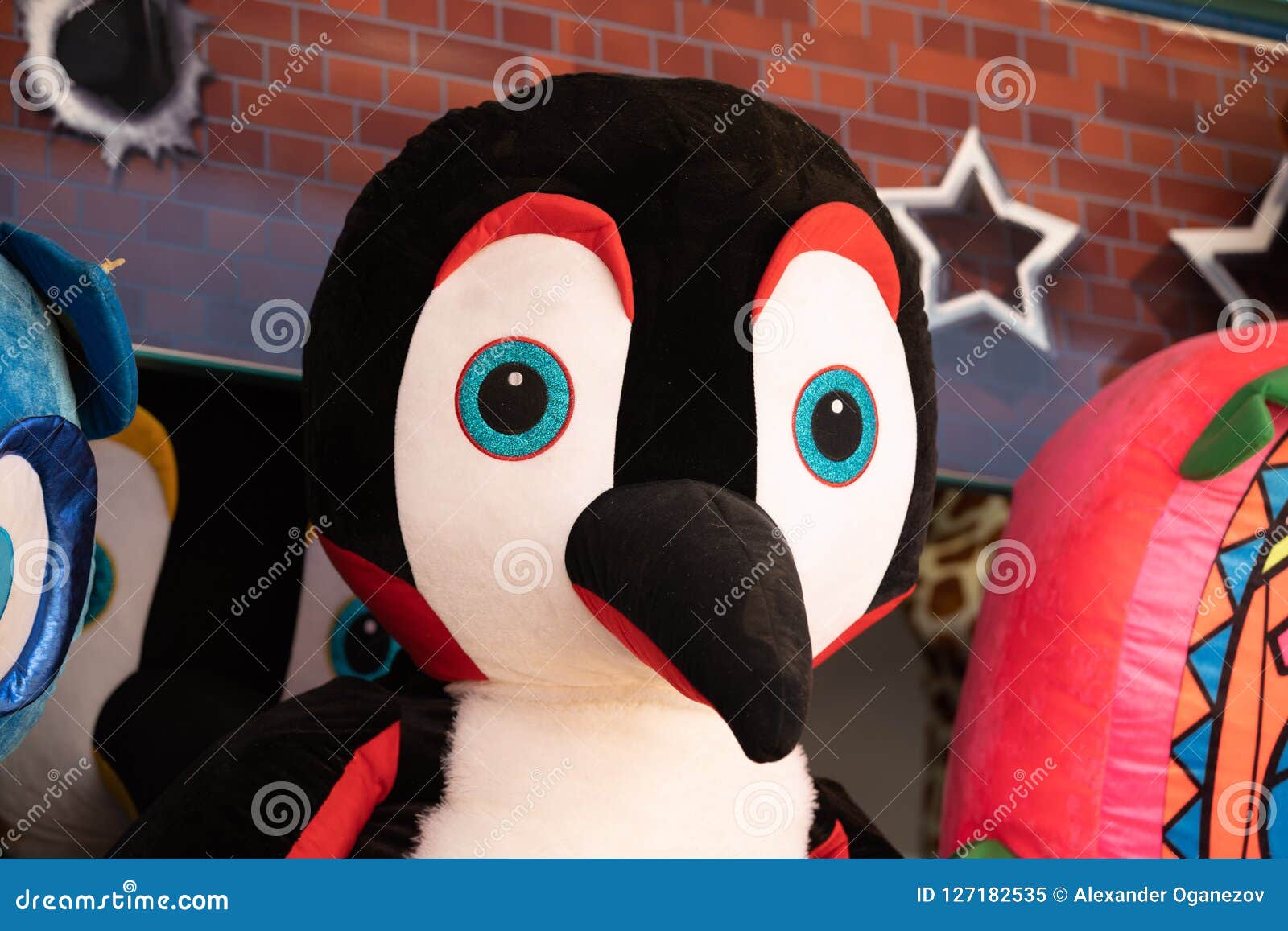 Giant plush penguin on the wall. Giant penguin plush toy hanging on a wall among other tyos at outdoors market fair.