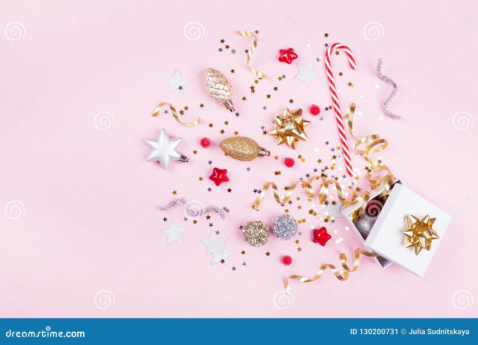 gift or present box with confetti stars, golden ribbon and holiday decoration on pastel pink background. christmas flat lay.