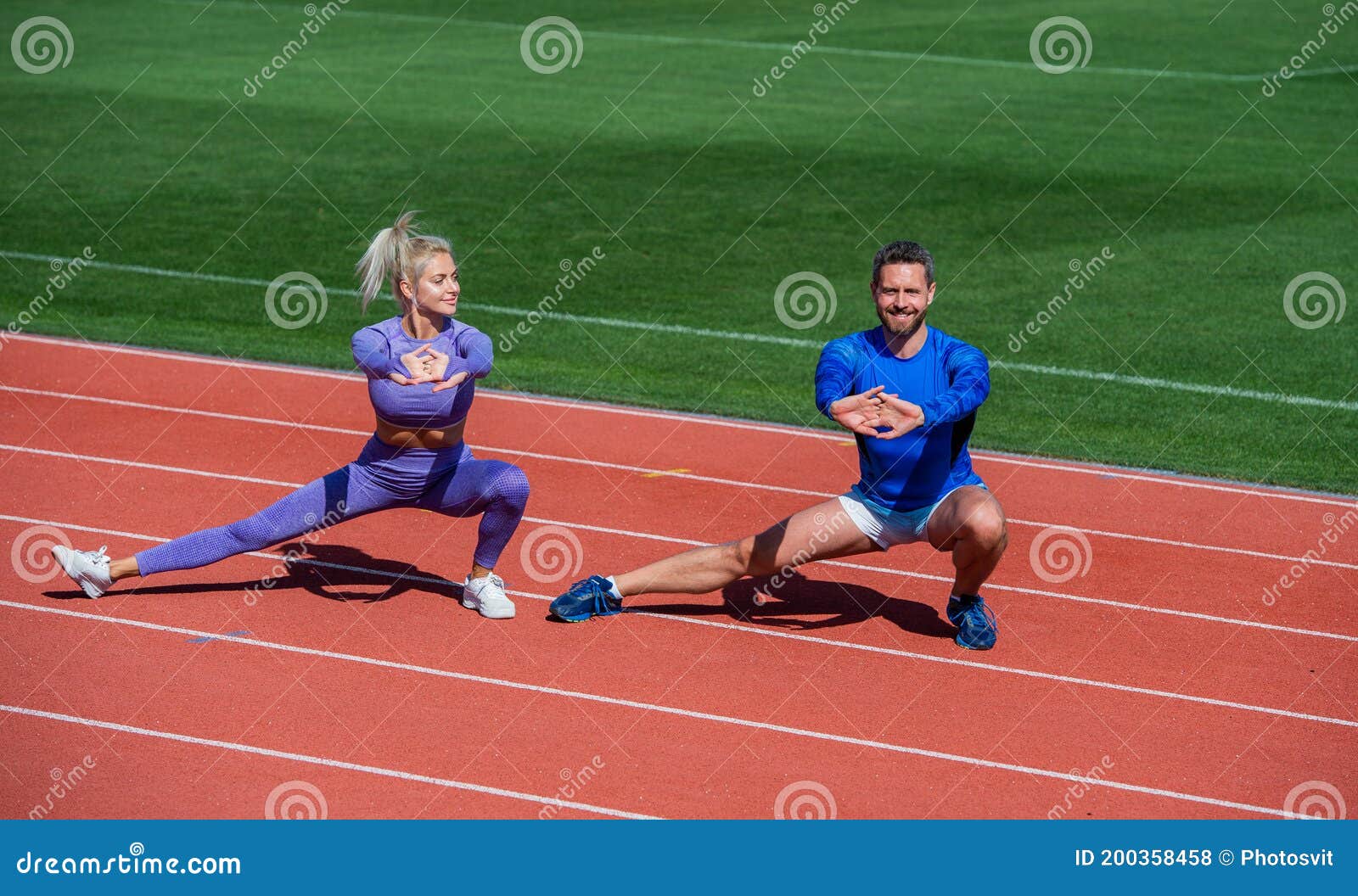 Hombres y mujeres jóvenes en ropa deportiva de pie en las pistas de  carreras del estadio al aire libre y haciendo ejercicio en conjunto
