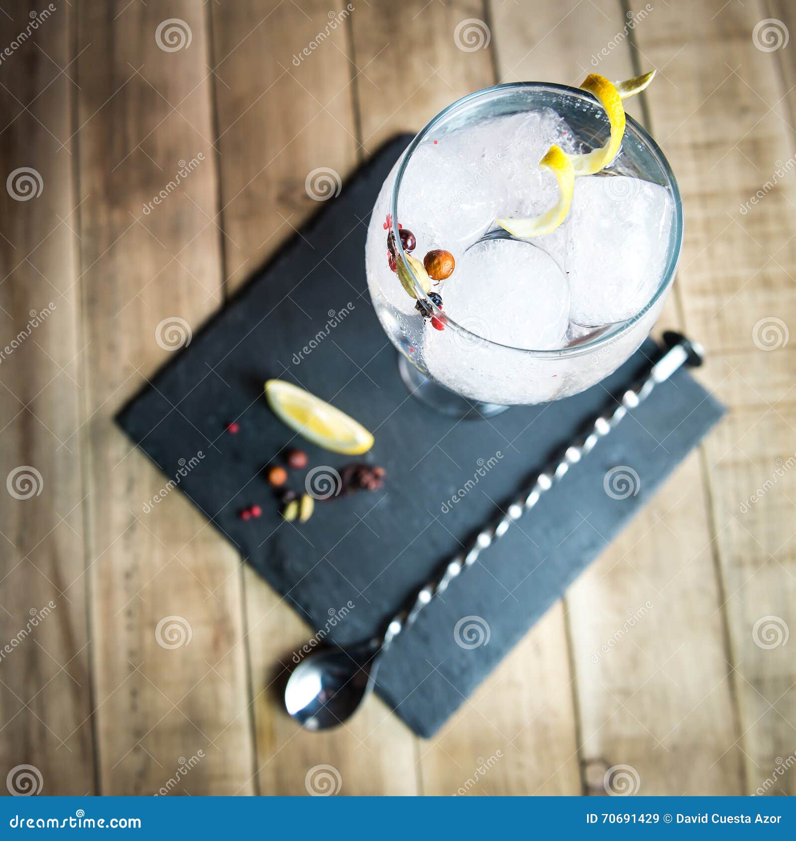 gin tonic with botanicals and bar spoon on wood table.