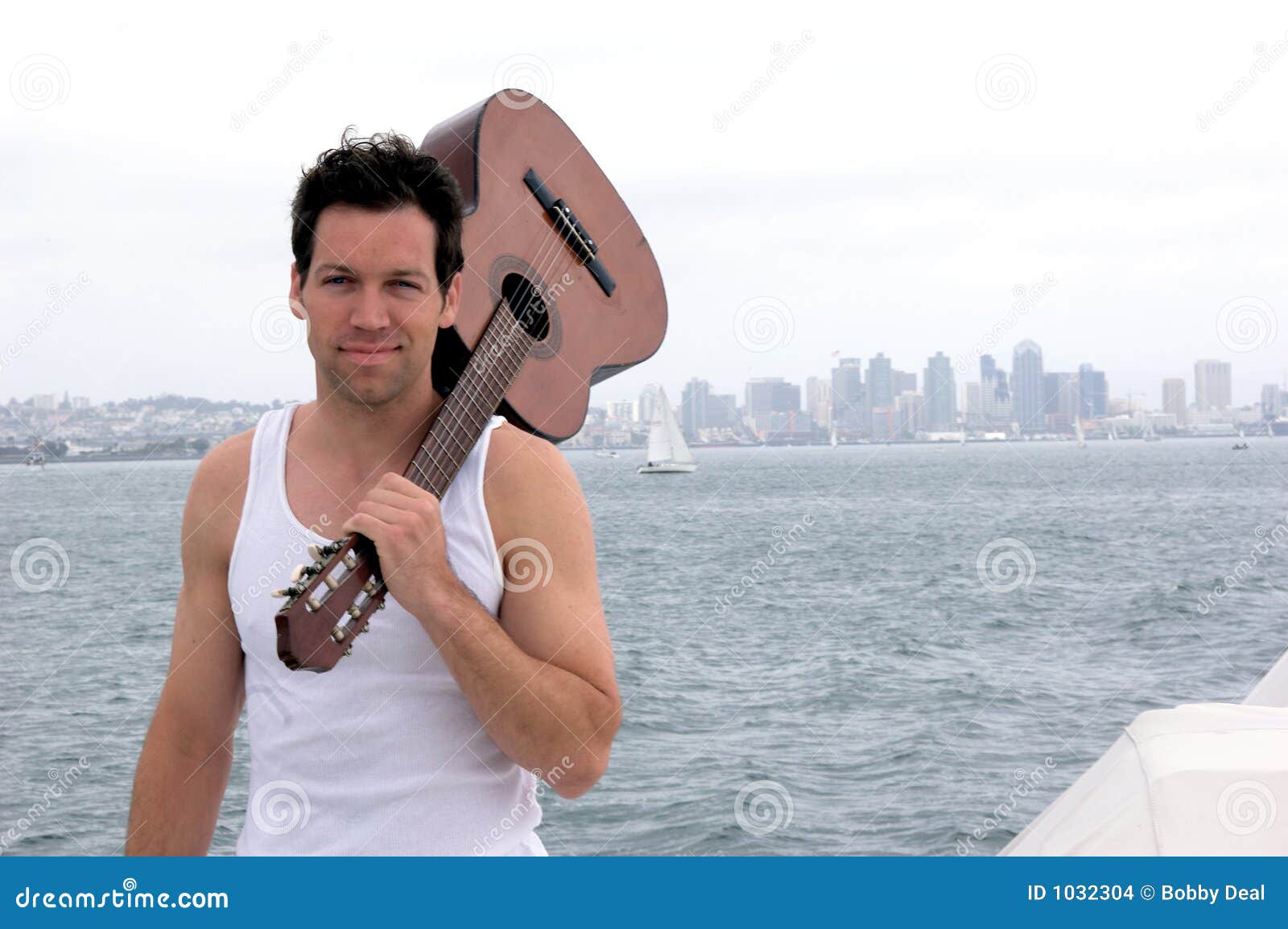 Giocatore di chitarra. Un giovane casuale con una chitarra accoustic su un yacht dentro nel porto di San Diego