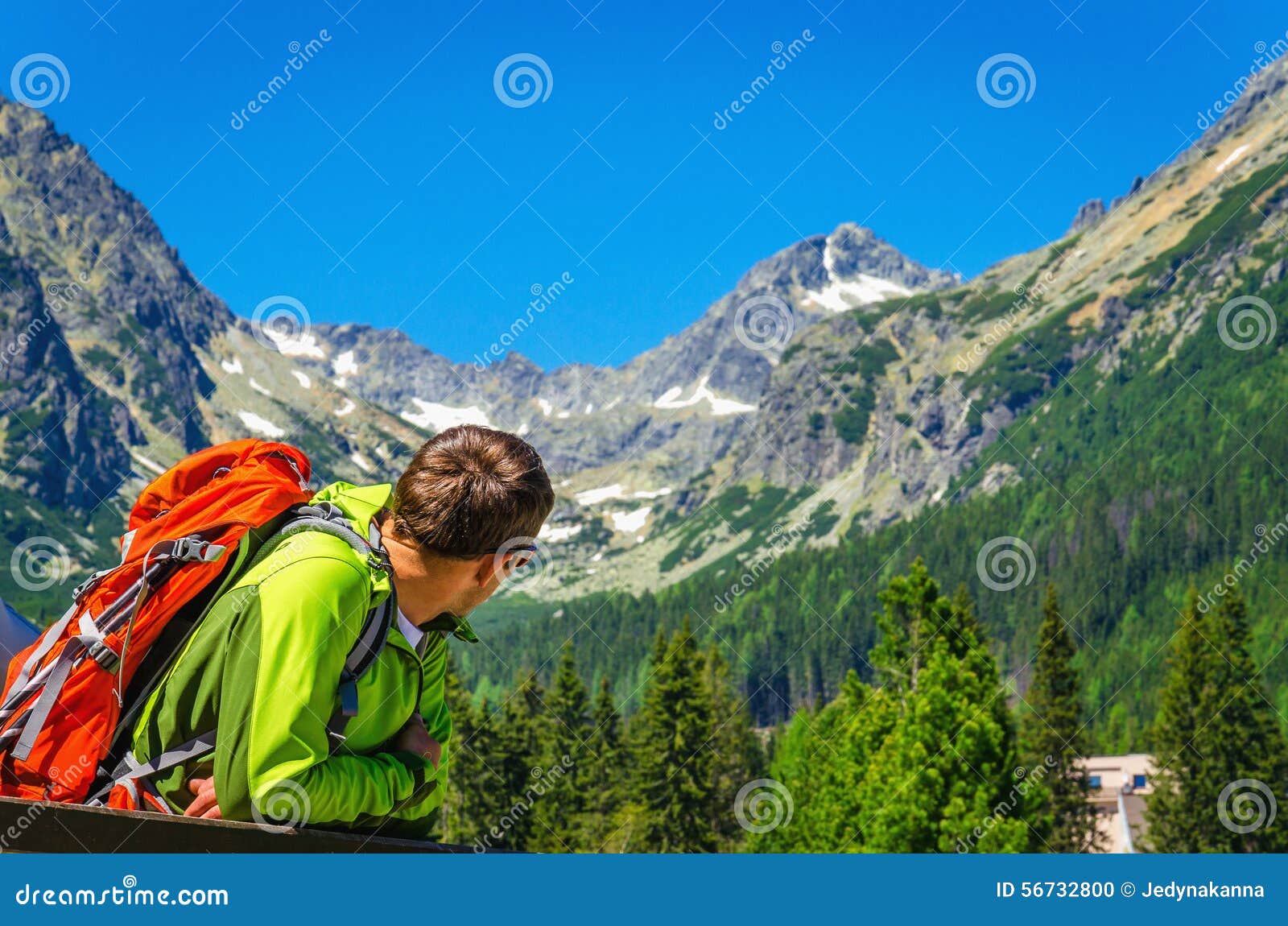 Giovane con lo zaino che esamina i picchi di montagna. Giovane con uno zaino arancio che esamina picchi i bei di montagna