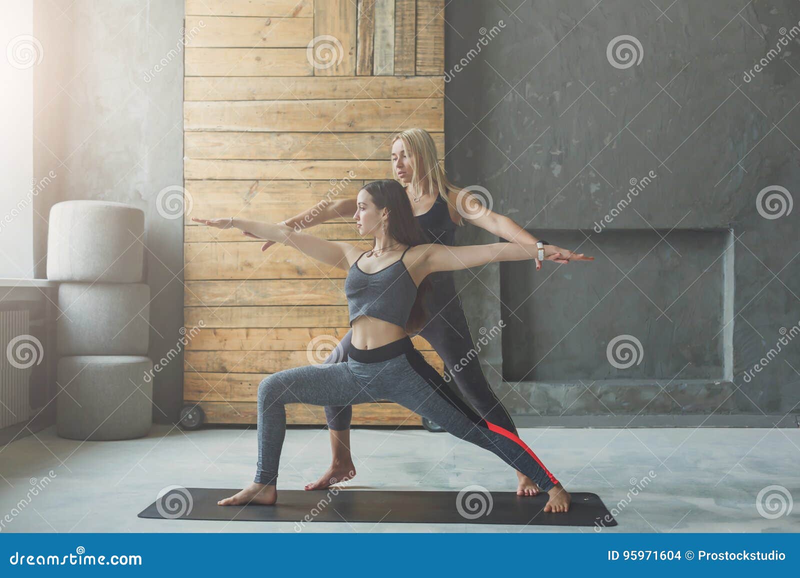 Giovane donna con l'istruttore di yoga nel club di forma fisica, posa del guerriero. L'insegnante ed il principiante di yoga nella classe, facente il asana si esercita Posa del guerriero, Virabhadrasana Stile di vita sano nel club di forma fisica Allungando con la vettura