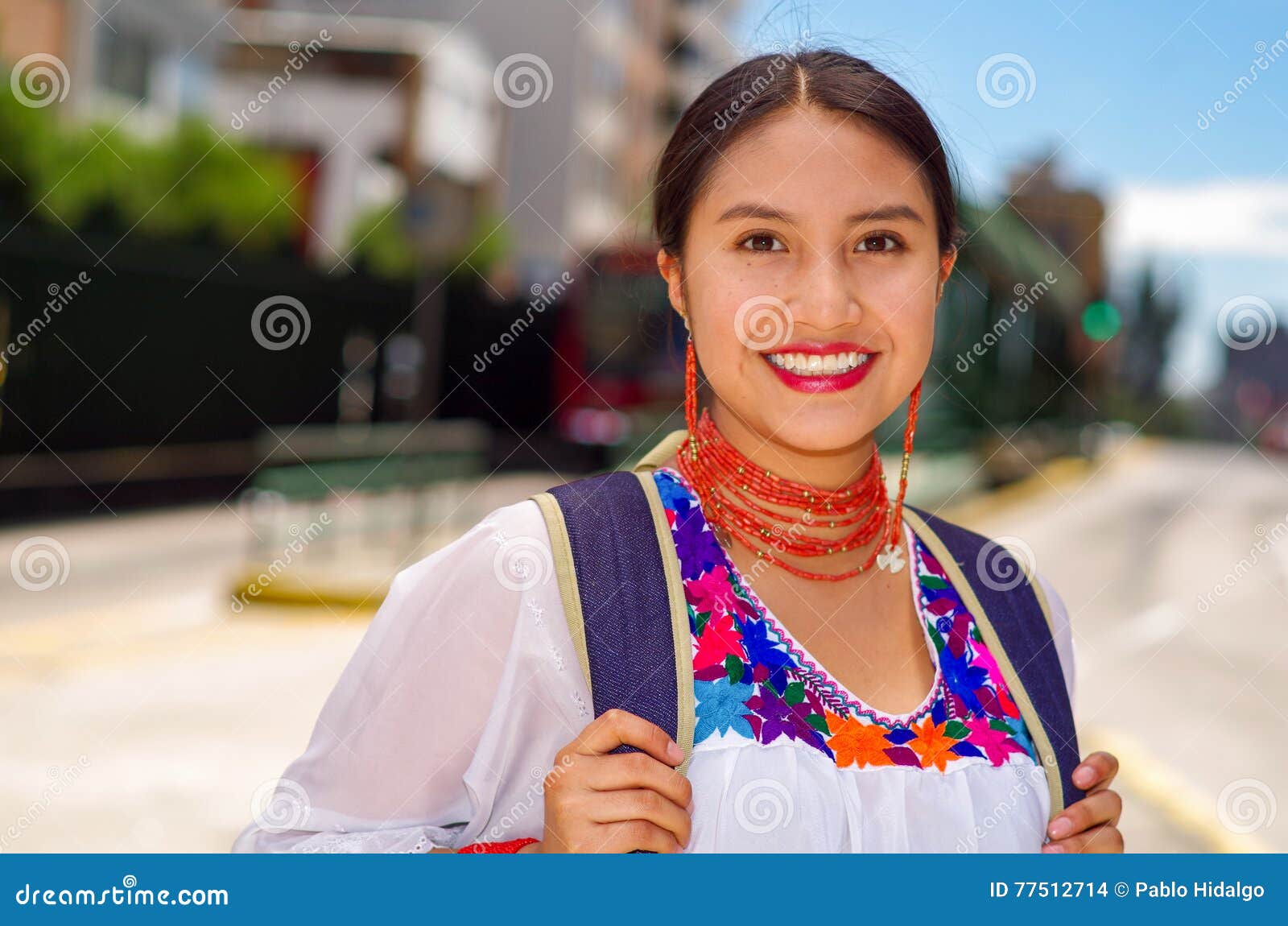 Giovane donna graziosa che indossa blusa andina tradizionale e zaino blu, bus aspettante al binario della stazione di aria aperta, sorridente felicemente