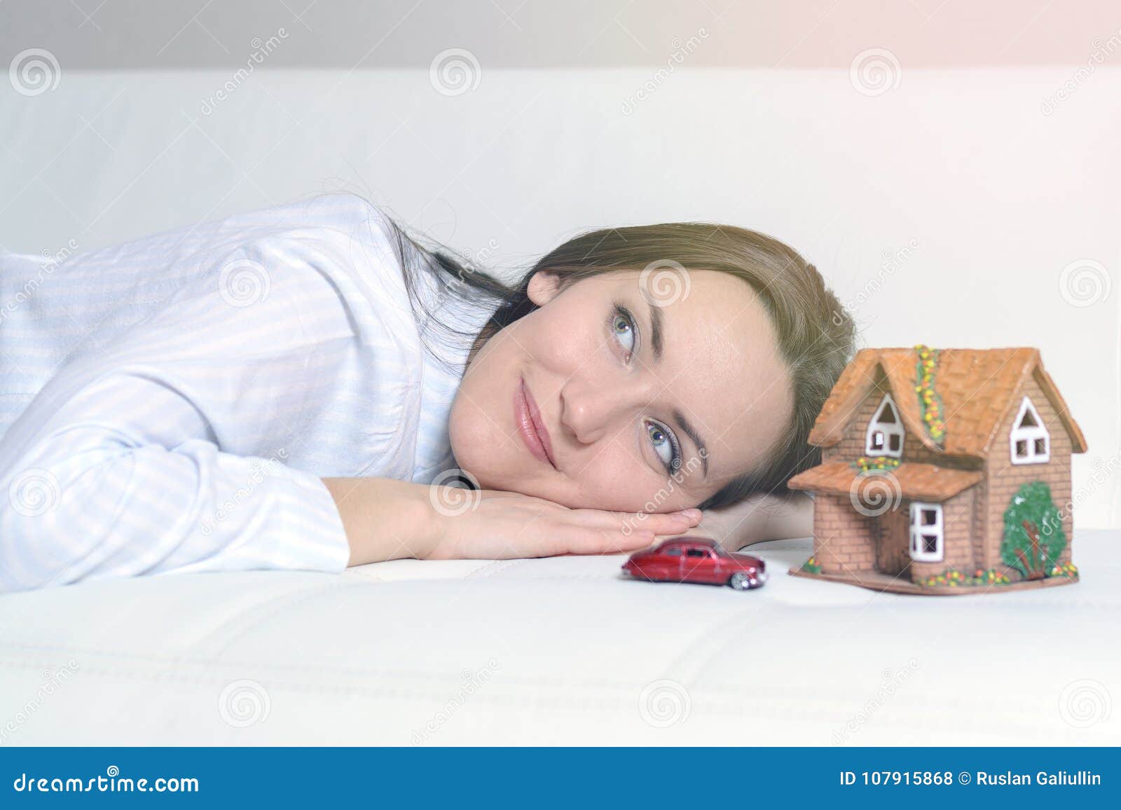 Giovane donna in pigiami che si trovano su un sofà bianco in una stanza davanti ad una casa di Wendy e un'automobile e sogni di un futuro luminoso